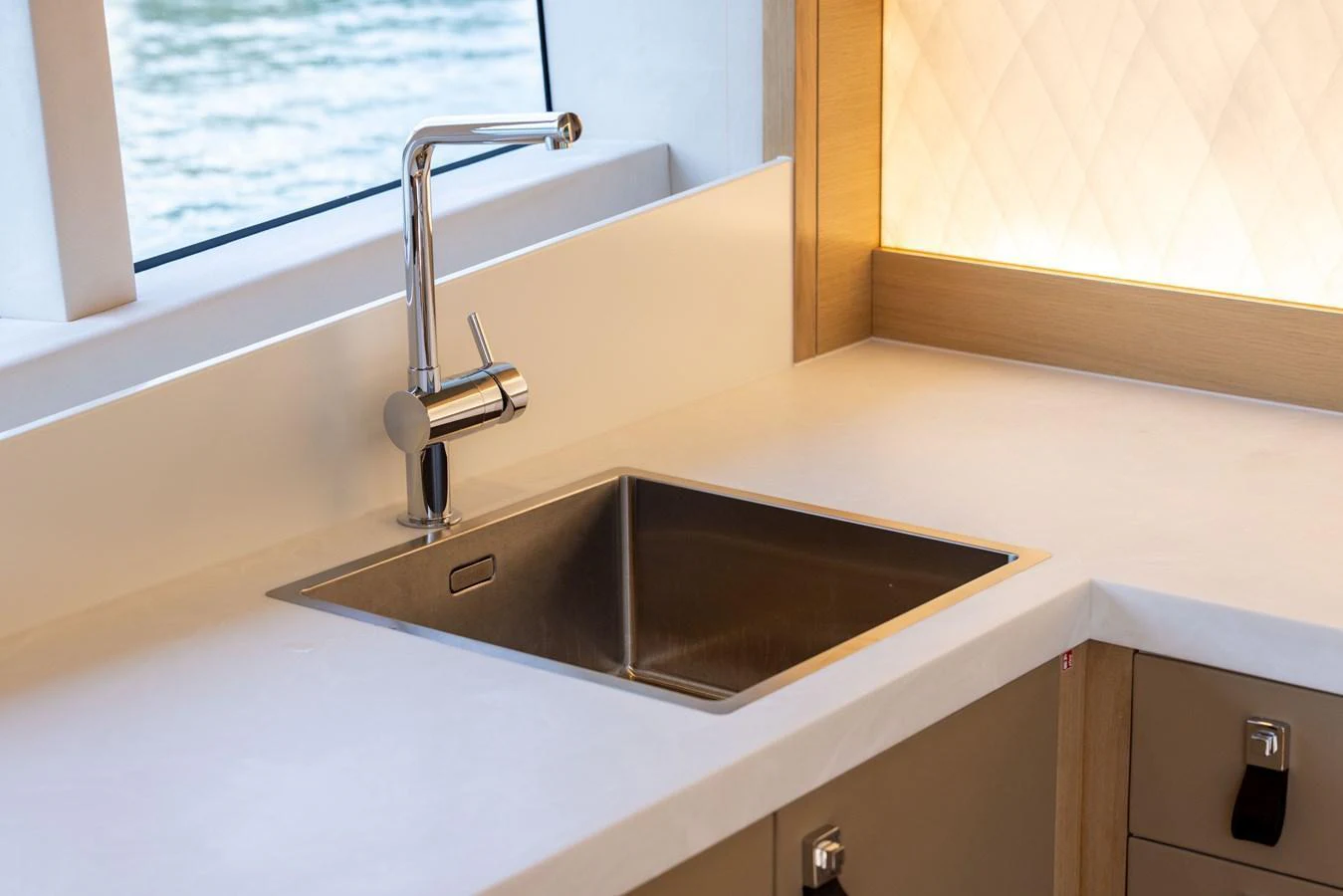 The yacht's galley features a sleek stainless steel sink with a modern faucet, set against a backdrop of elegant cabinetry and a view of the water. aboard GRIT Yacht for Sale