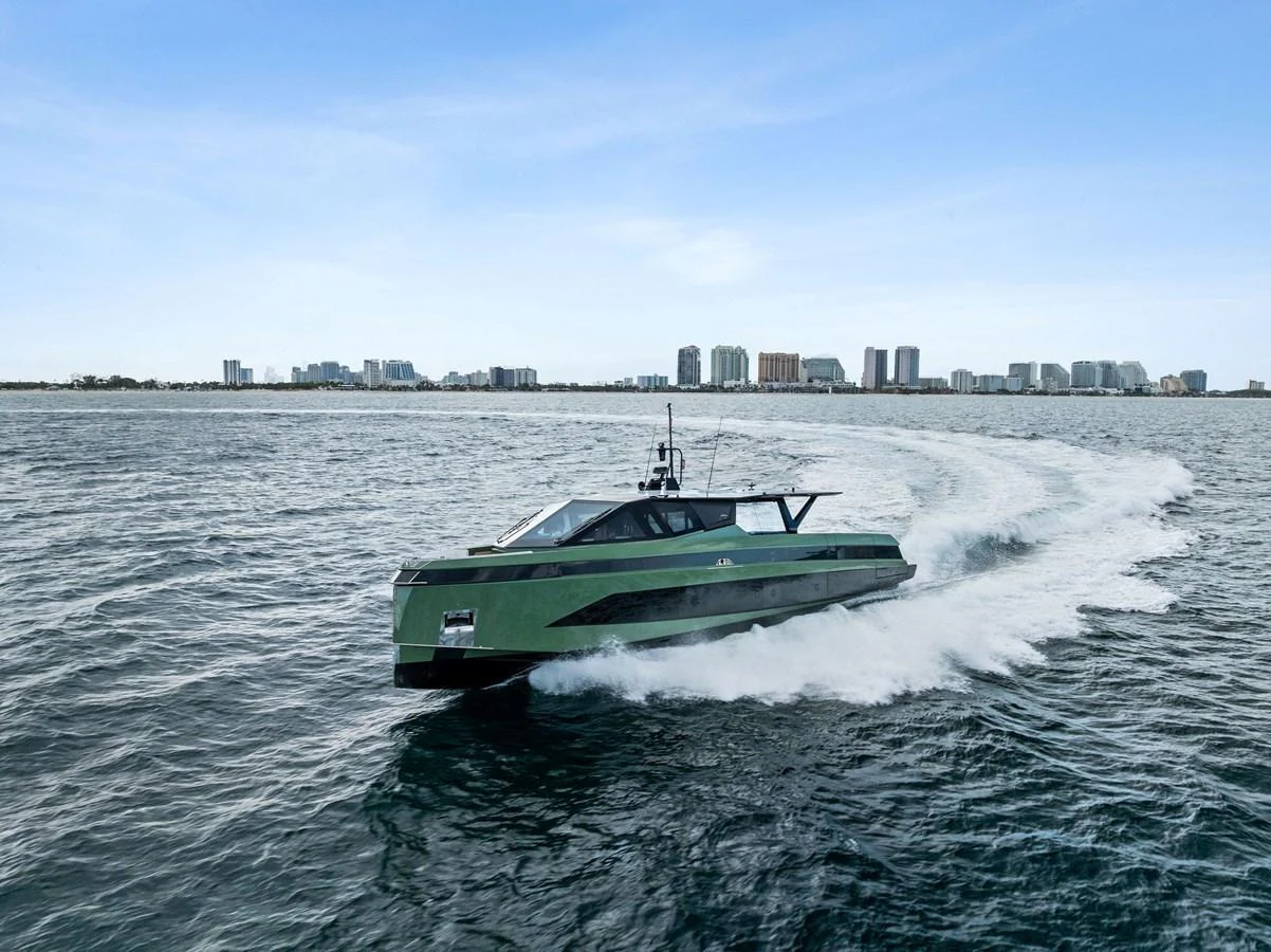 A sleek, modern yacht cruises swiftly through open waters with a cityscape in the background. aboard ANOTHER WORLD Yacht for Sale