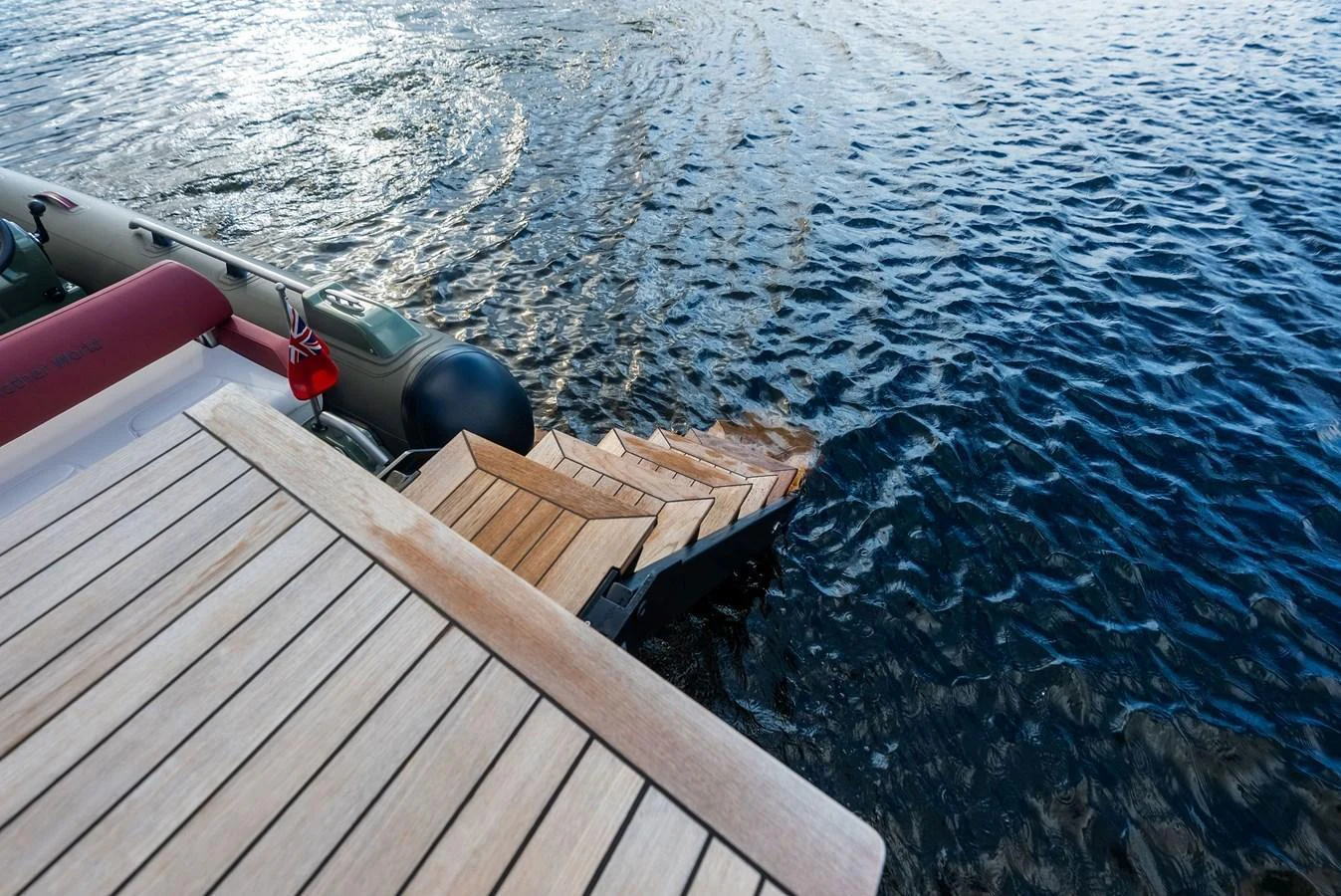 The image captures a yacht's swim platform with wooden steps leading down to the water. aboard ANOTHER WORLD Yacht for Sale