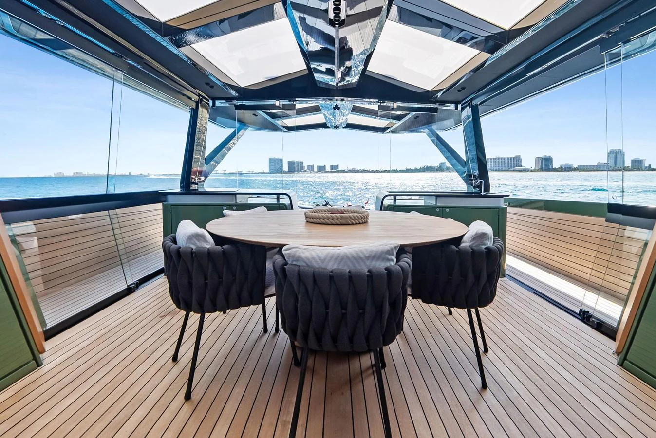 The aft deck features a stylish dining area with a round table and plush seating, offering stunning views of the water. aboard ANOTHER WORLD Yacht for Sale