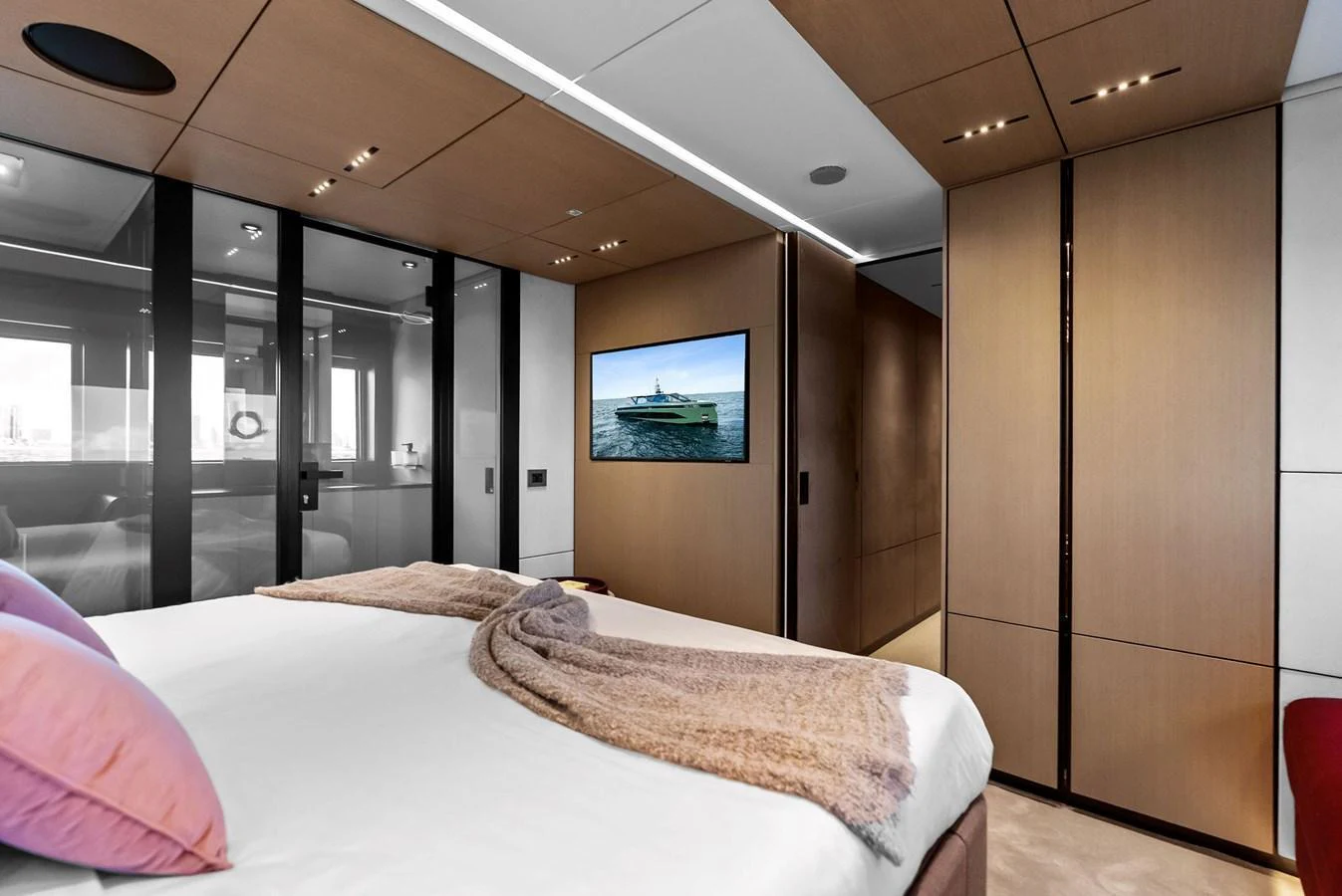 The stateroom features a luxurious bed with a soft throw, modern wood paneling, and a flat-screen TV. aboard ANOTHER WORLD Yacht for Sale