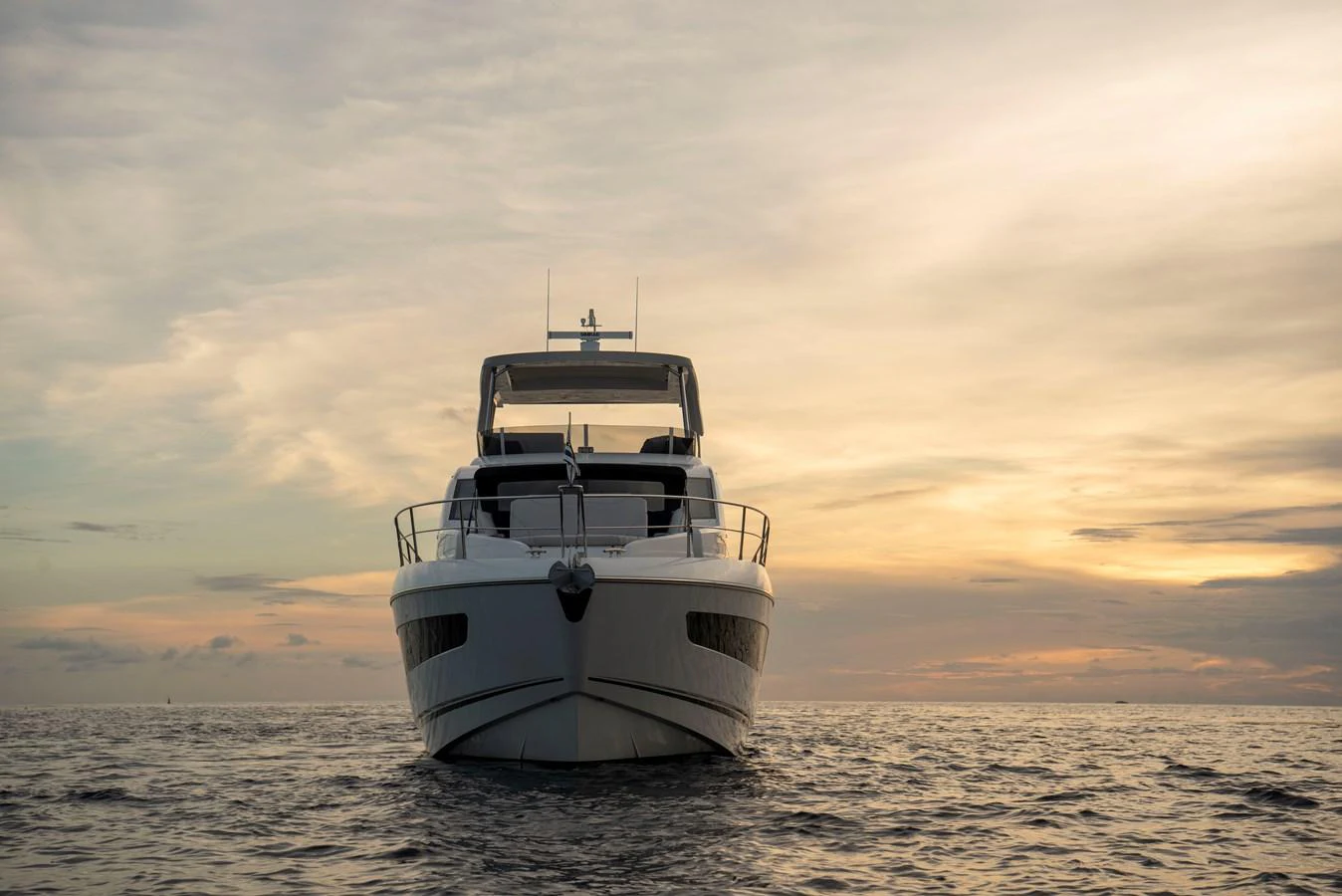 A sleek yacht is captured head-on against a serene sunset backdrop on the open water. aboard GAIA Yacht for Sale