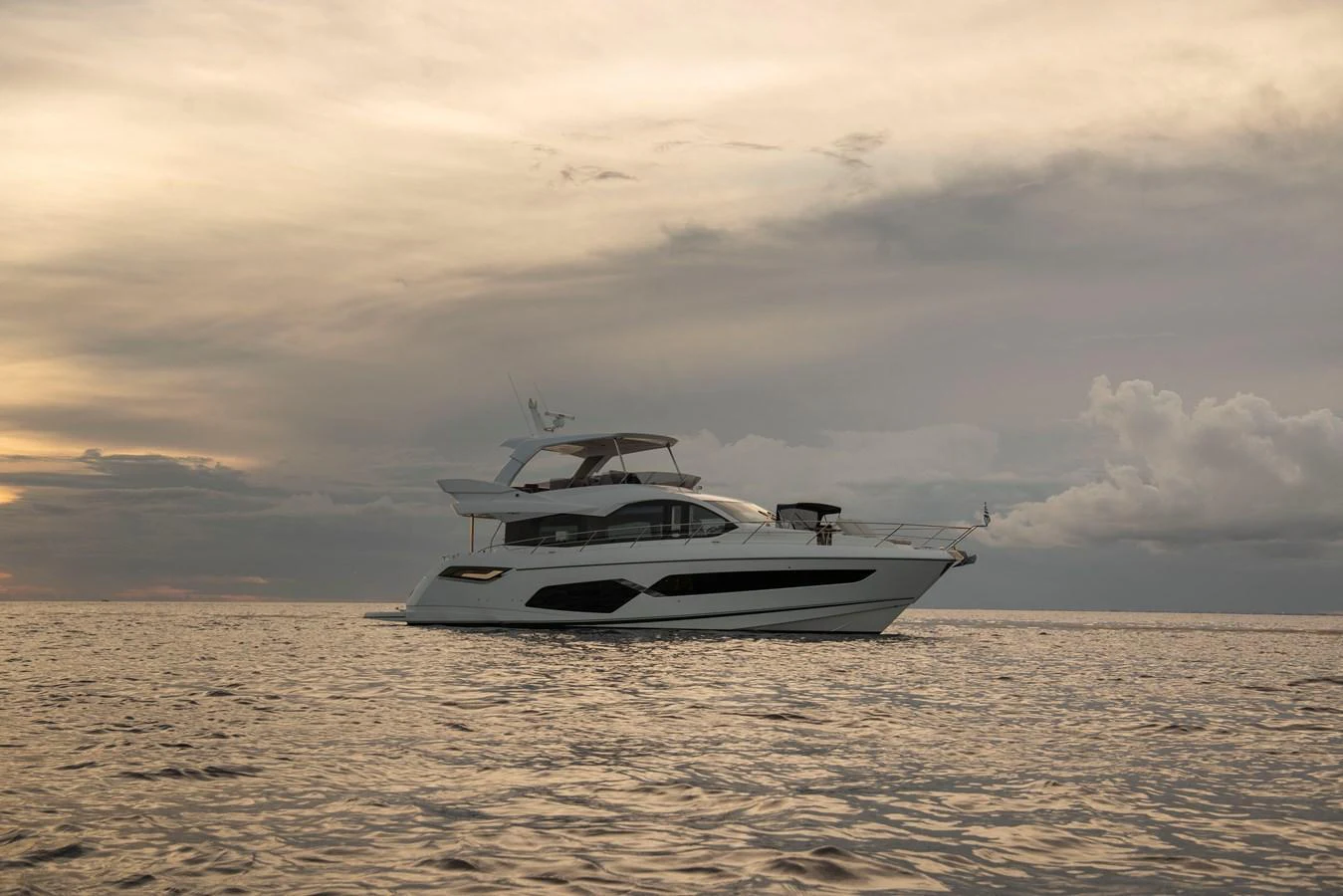 A sleek yacht cruises serenely on calm waters under a dramatic sky. aboard GAIA Yacht for Sale