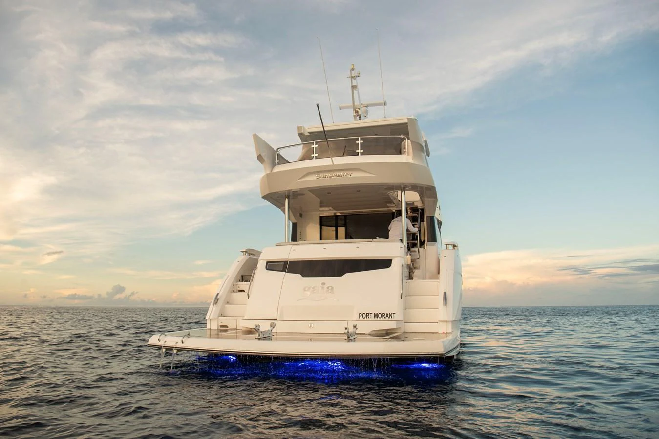 A luxurious yacht is seen from the rear, illuminated by underwater lights as it floats on calm waters at sunset. aboard GAIA Yacht for Sale