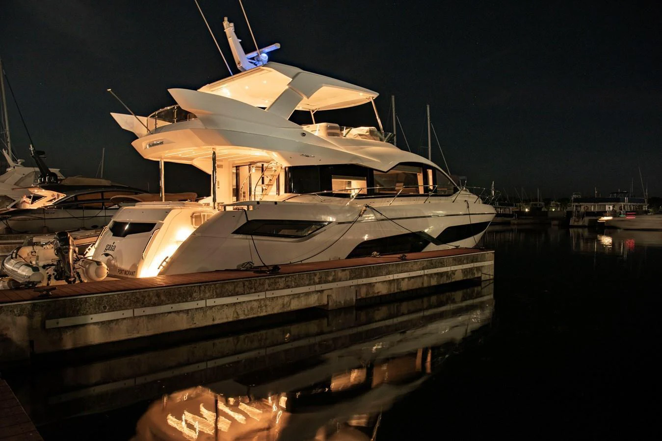 A sleek and modern yacht is docked at night, illuminated by warm lights. aboard GAIA Yacht for Sale