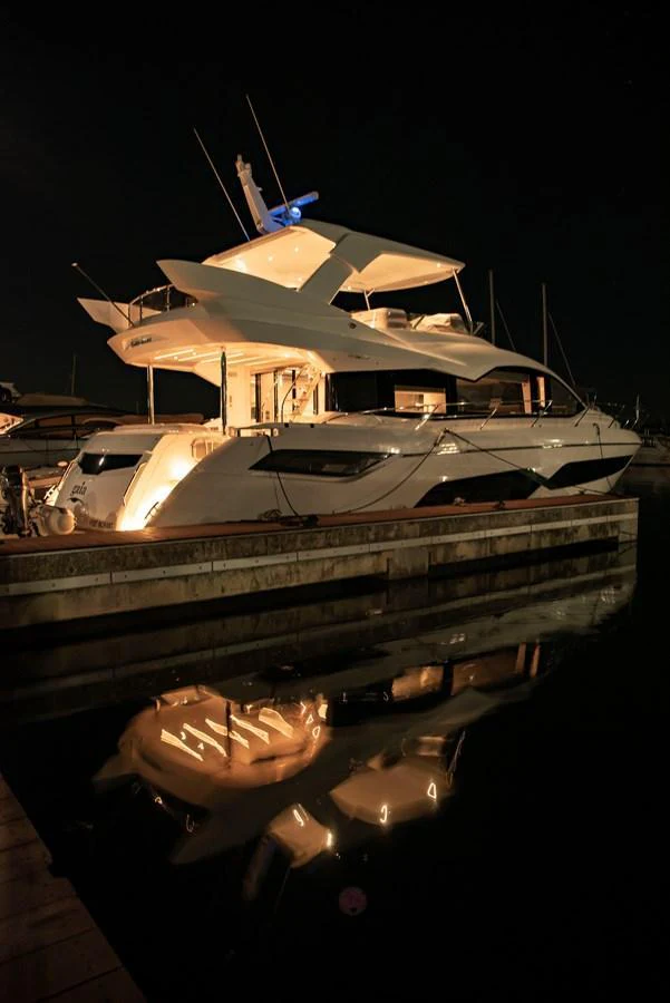 A sleek yacht is beautifully illuminated at night, docked in a serene marina. aboard GAIA Yacht for Sale