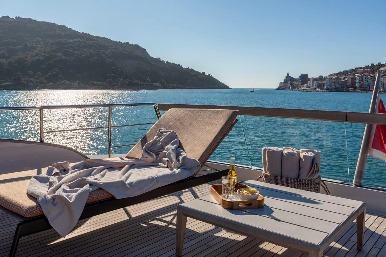 The sundeck offers a serene spot with a sun lounger and a table set with refreshments, overlooking a picturesque coastal view. aboard QUEEN MARTINA Yacht for Sale