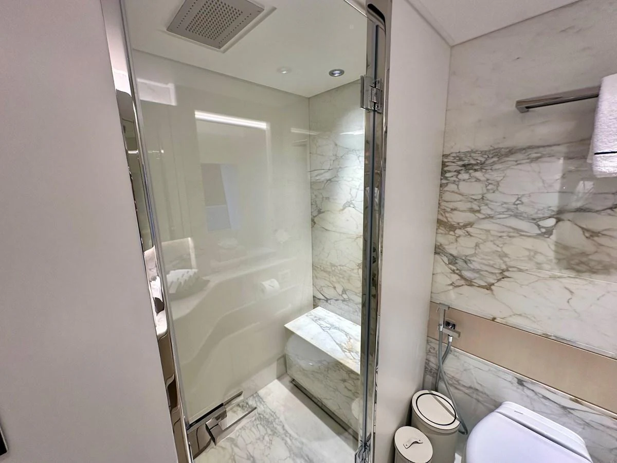 The yacht's bathroom features a sleek, modern design with marble accents and a glass-enclosed shower. aboard OPTIMISM Yacht for Sale