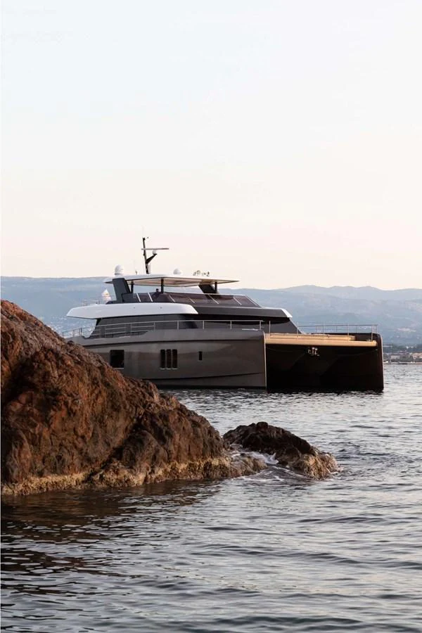 A sleek yacht glides gracefully on calm waters near rocky shores. aboard 80 SUNREEF POWER NEXT Yacht for Sale