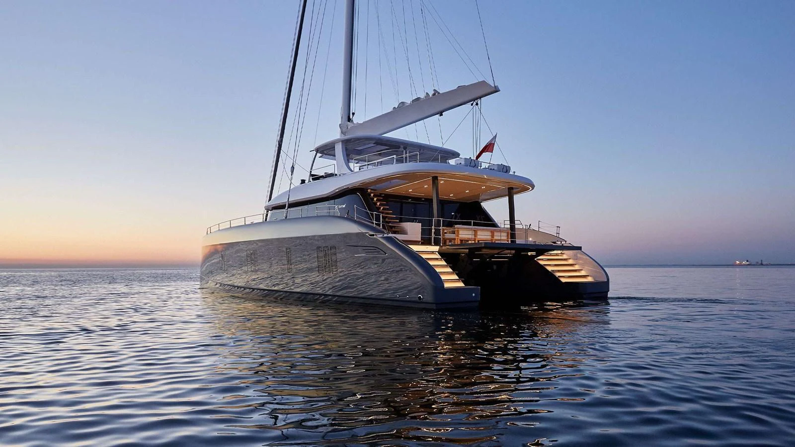 A luxurious catamaran yacht is anchored at sunset, showcasing its elegant design and illuminated aft deck. aboard SUNREEF 80 NEXT Yacht for Sale