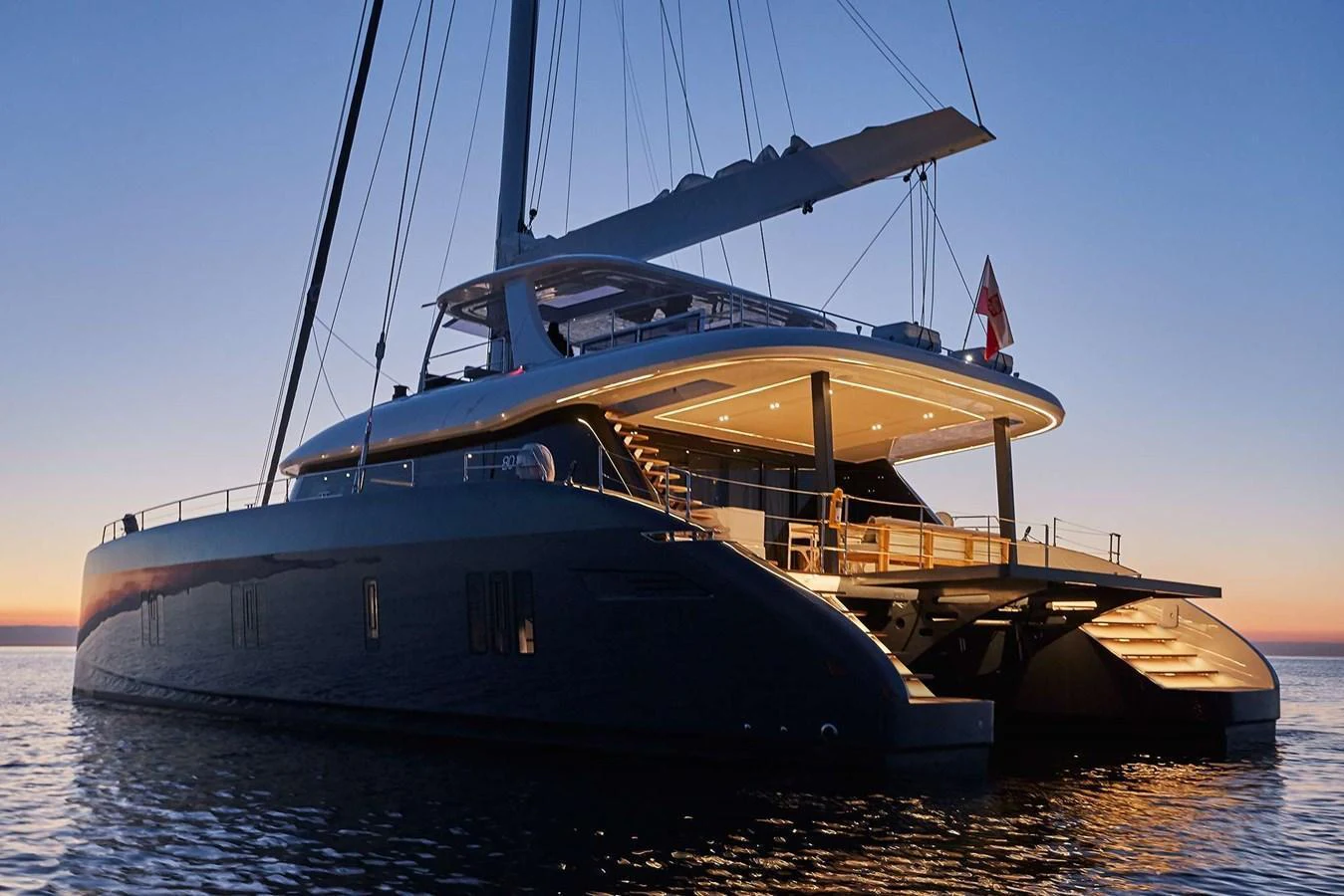A luxurious catamaran yacht is beautifully illuminated at dusk, showcasing its sleek design and spacious decks. aboard SUNREEF 80 NEXT Yacht for Sale