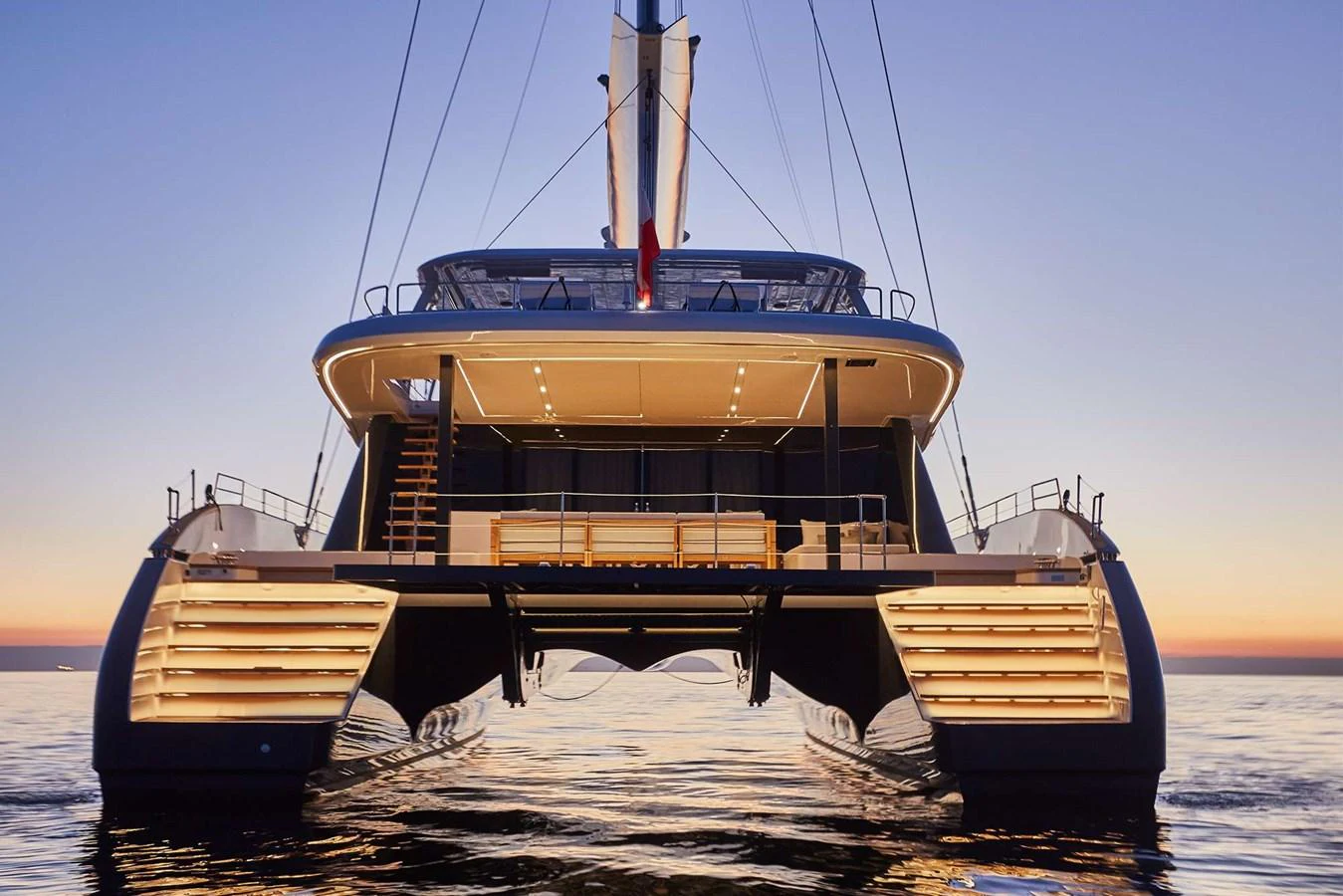 A stunning catamaran yacht is illuminated against a serene sunset backdrop, showcasing its sleek design and inviting aft deck. aboard SUNREEF 80 NEXT Yacht for Sale