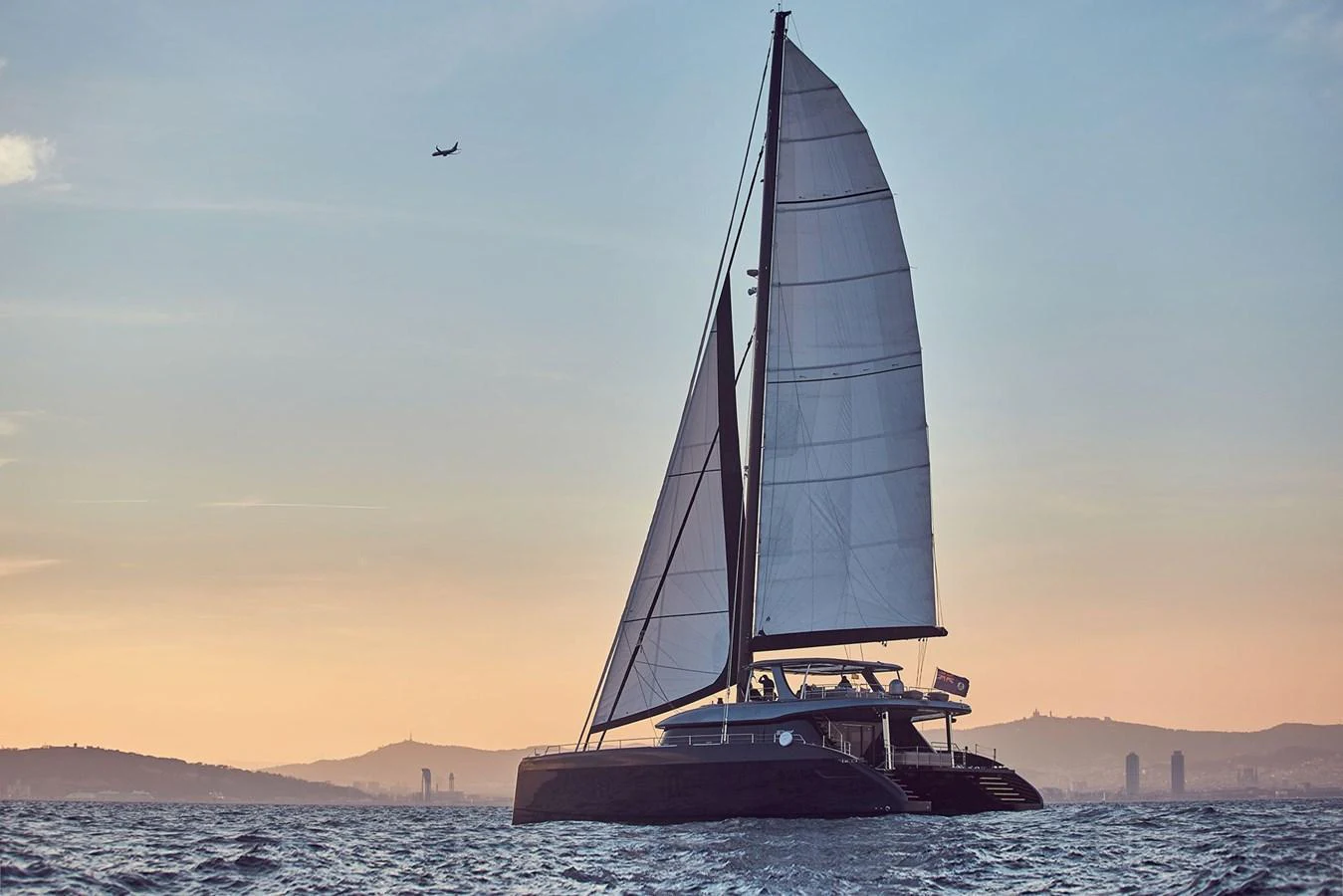 A sleek sailing yacht glides gracefully on the water at sunset. aboard SUNREEF 80 NEXT Yacht for Sale
