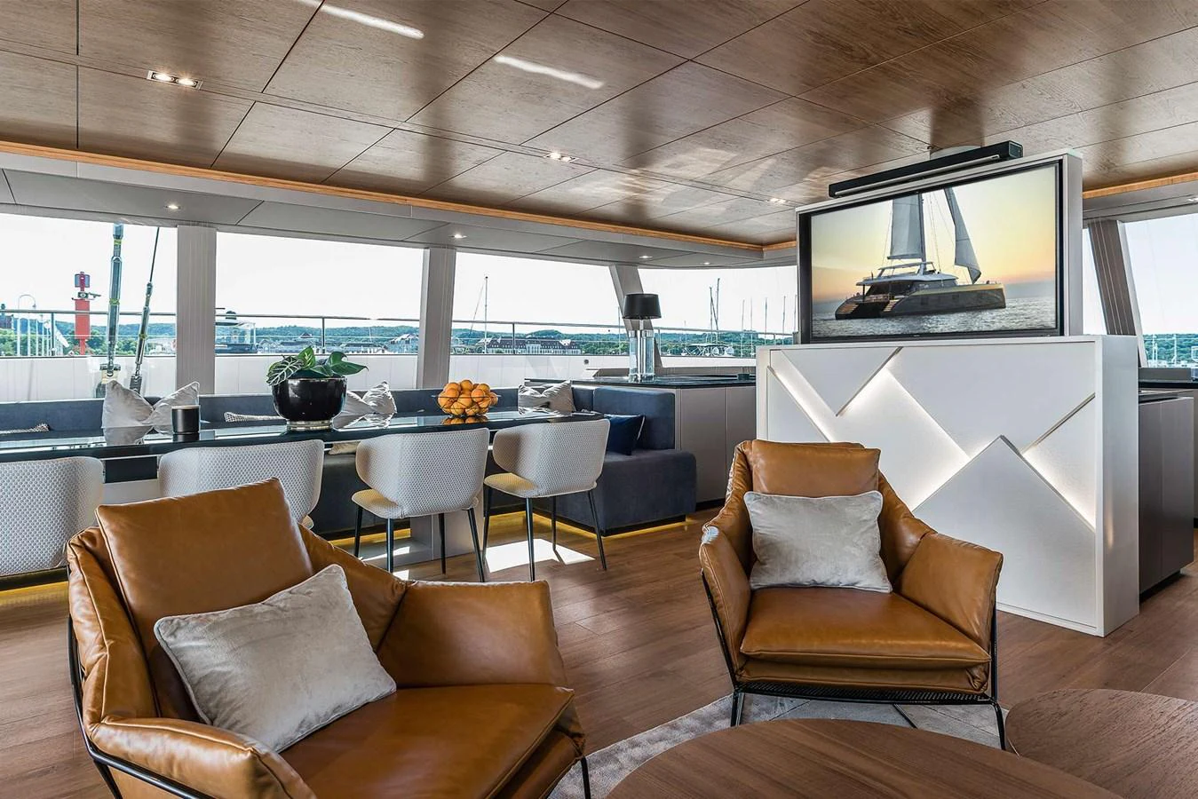 The salon features luxurious seating and a large TV with a view of the marina through expansive windows. aboard SUNREEF 80 NEXT Yacht for Sale