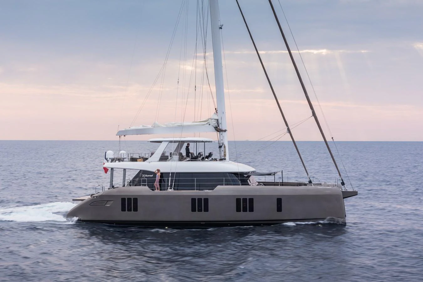A sleek and modern catamaran yacht glides smoothly across calm waters at sunset. aboard SUNREEF 70 NEXT Yacht for Sale