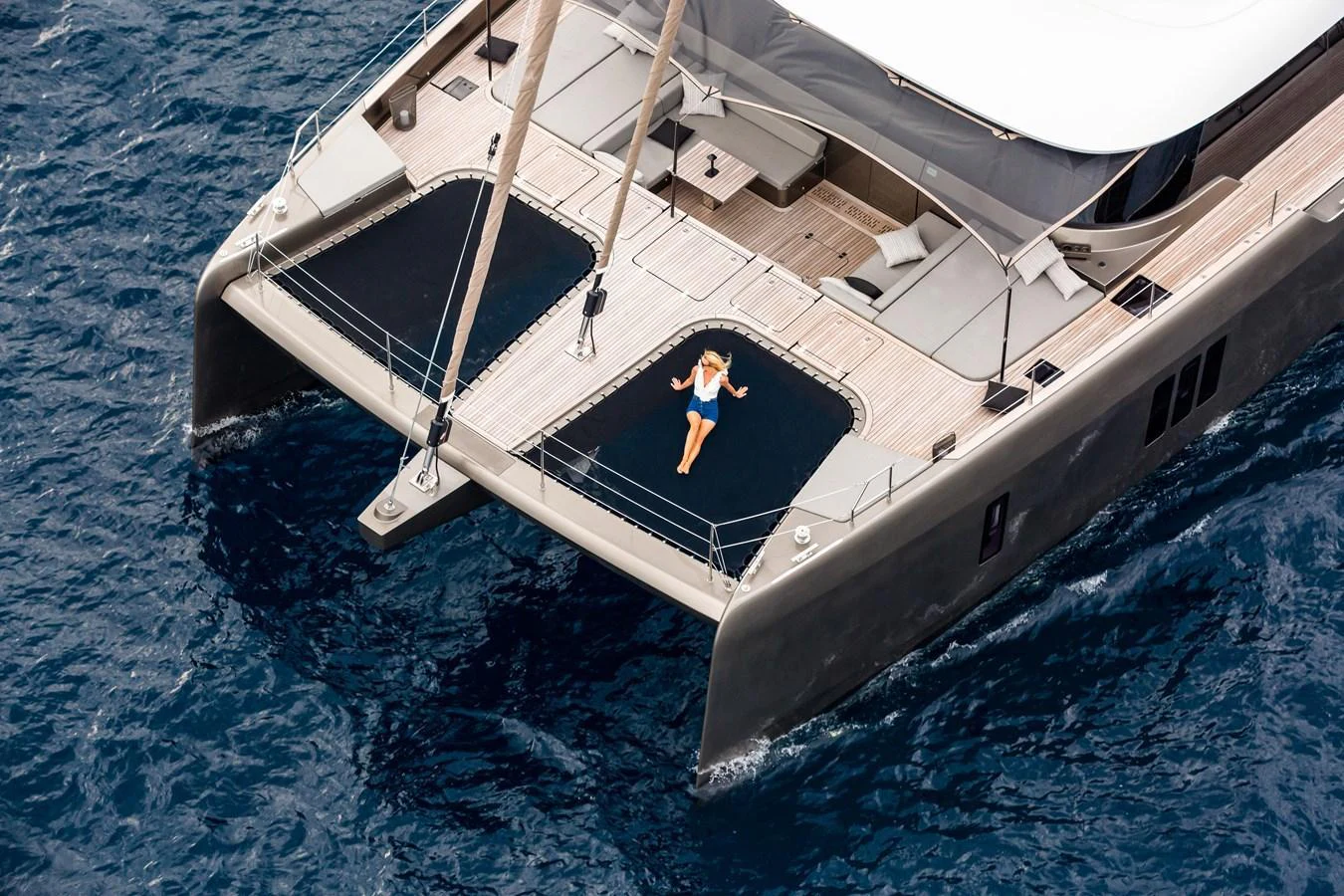 A luxurious catamaran yacht with a spacious deck and a person relaxing on the netting over the water. aboard SUNREEF 70 NEXT Yacht for Sale