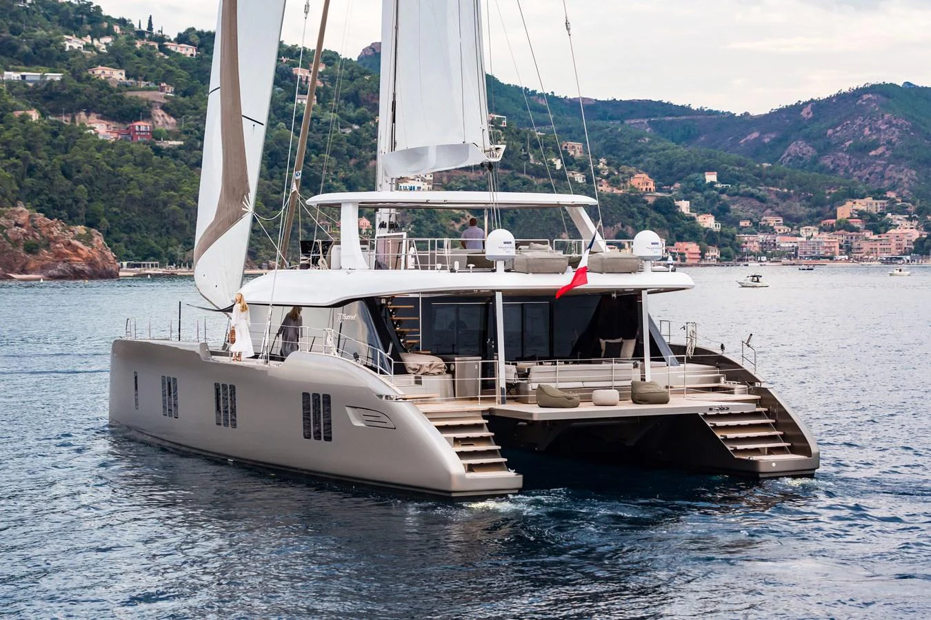 A luxurious catamaran yacht is anchored in a scenic coastal area with lush hills in the background. aboard SUNREEF 70 NEXT Yacht for Sale