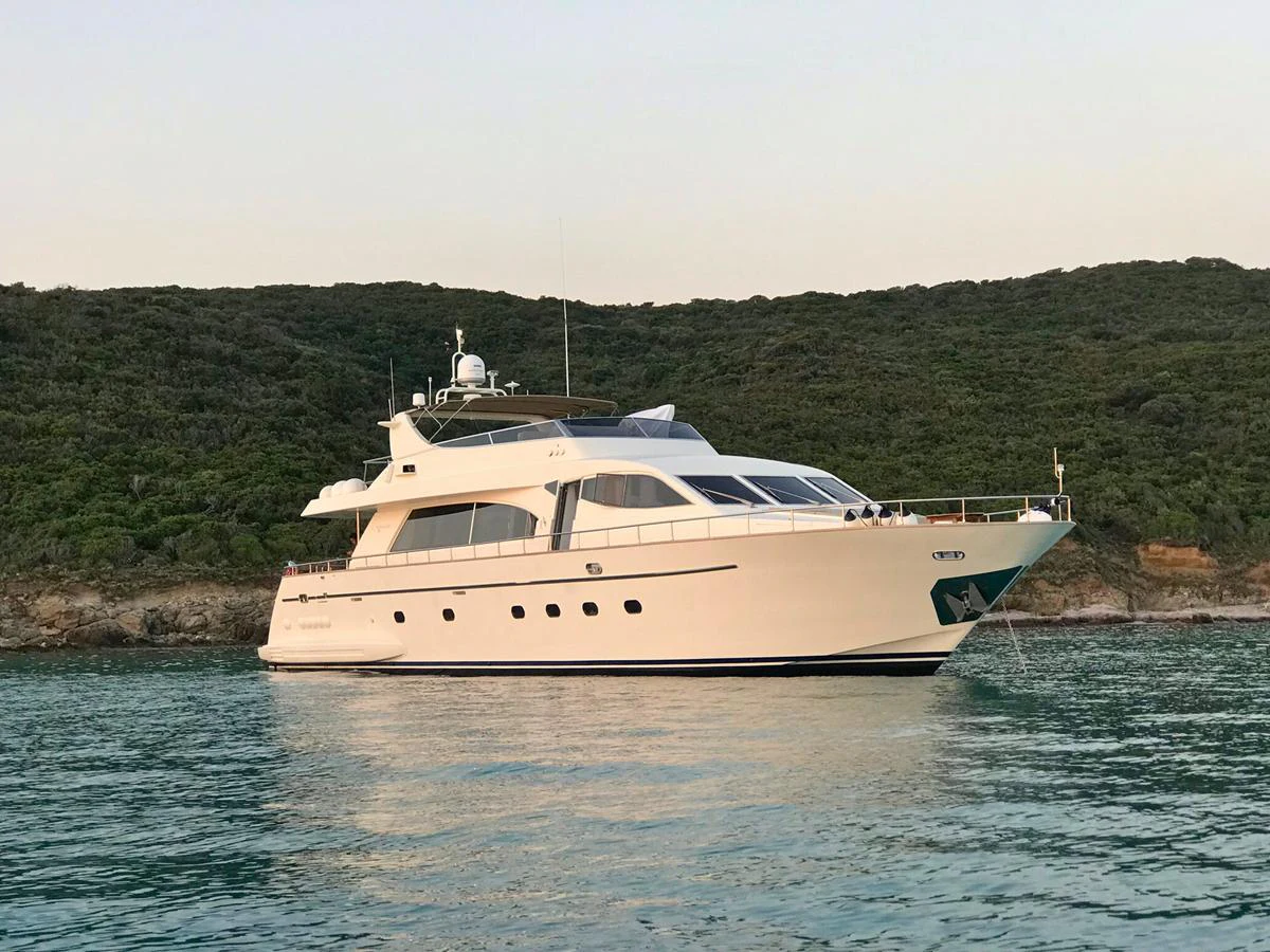 A sleek and elegant yacht is anchored in calm waters against a backdrop of lush greenery. aboard SIKOY Yacht for Sale