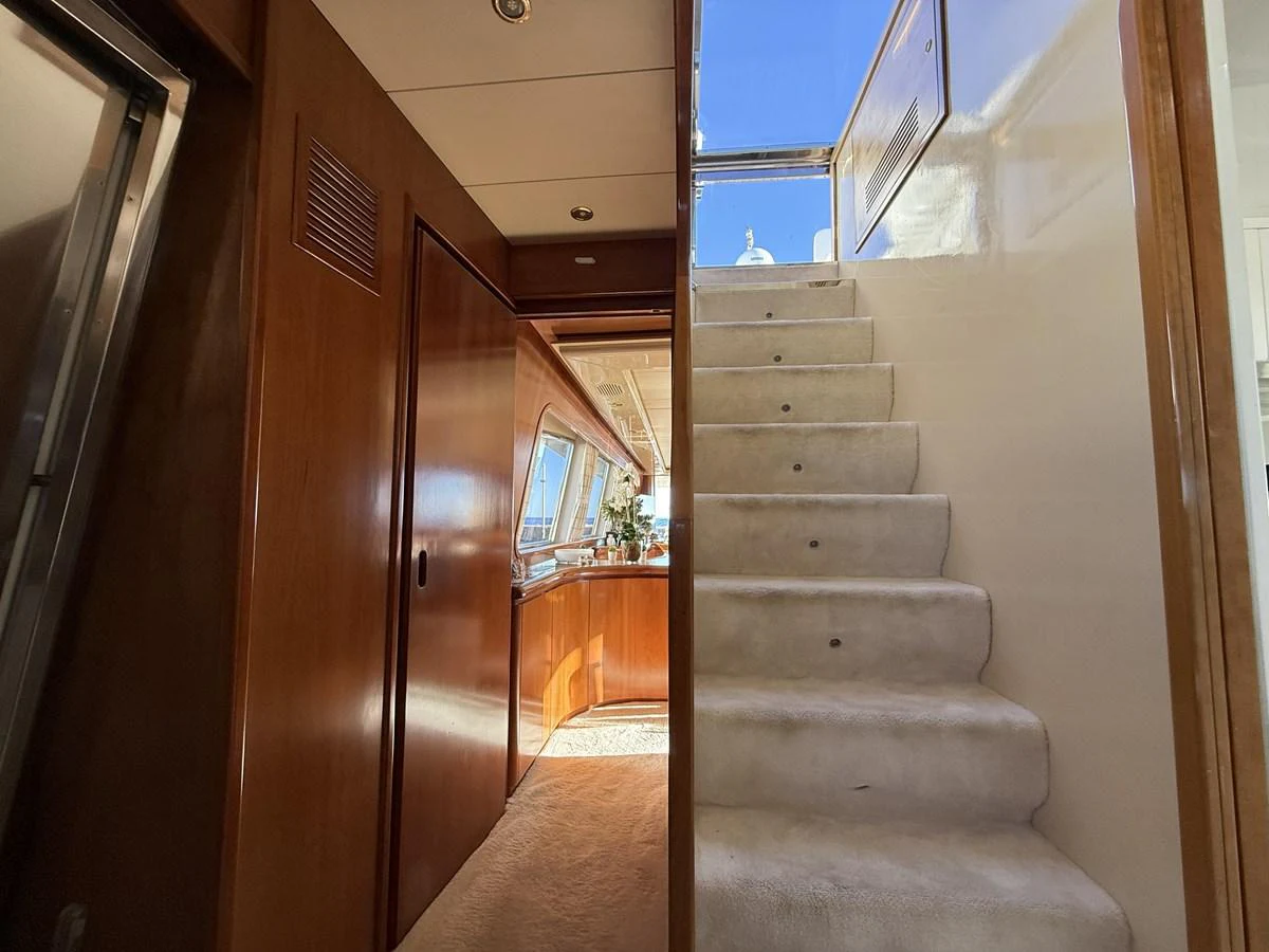 The image showcases a well-lit interior staircase leading to an upper deck, with polished wooden walls and a glimpse of a cozy seating area. aboard SIKOY Yacht for Sale