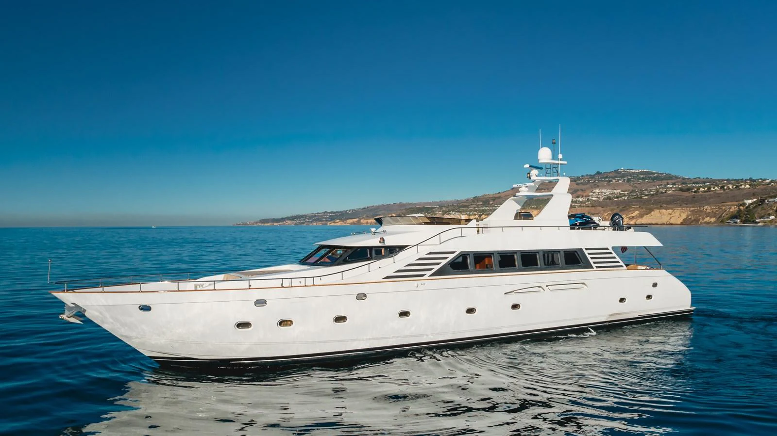 A sleek and elegant yacht glides smoothly on calm waters with a scenic coastline in the background. aboard MONEY CAT Yacht for Sale