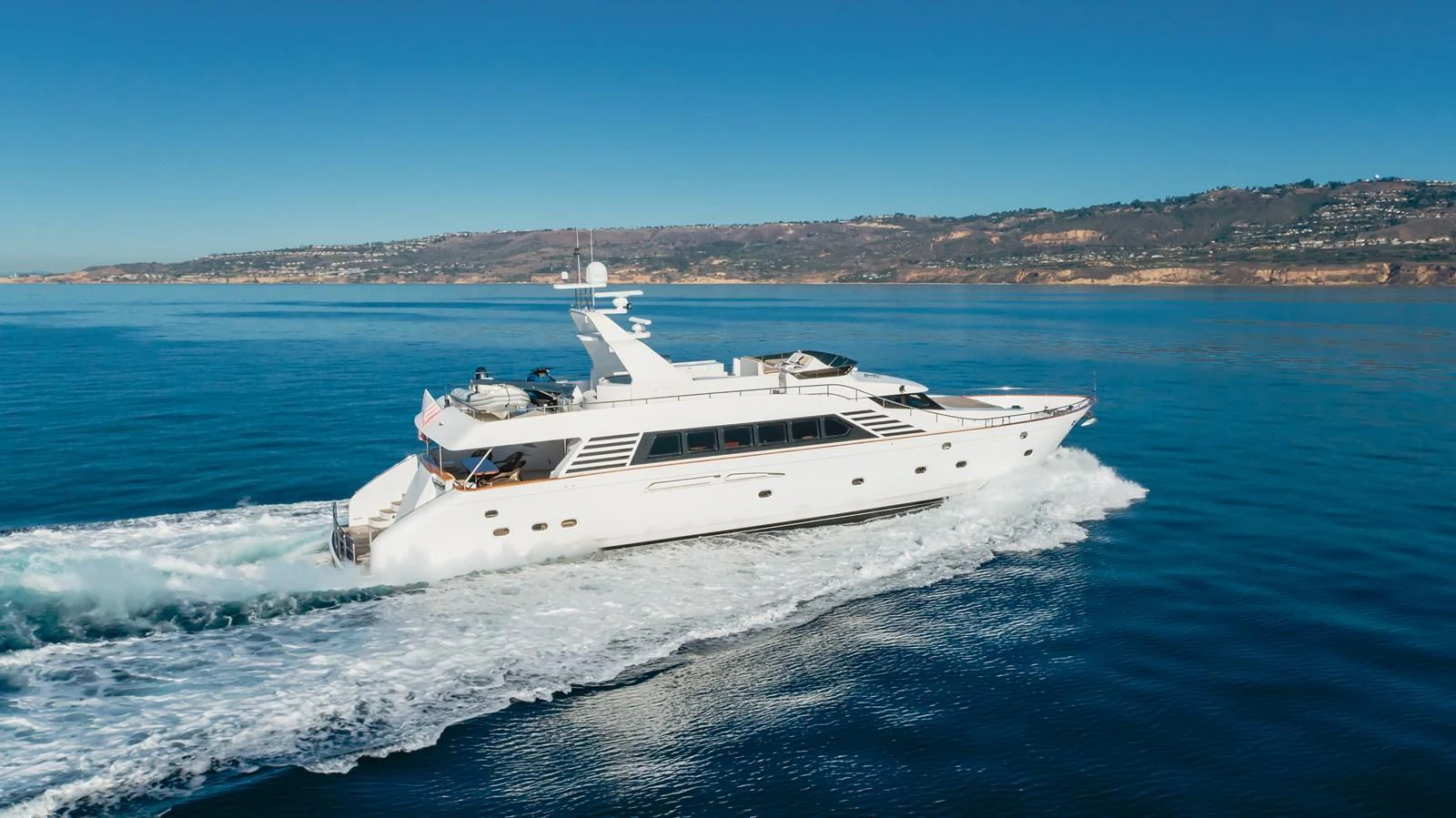 A sleek white yacht cruises through calm blue waters with a scenic coastline in the background. aboard MONEY CAT Yacht for Sale