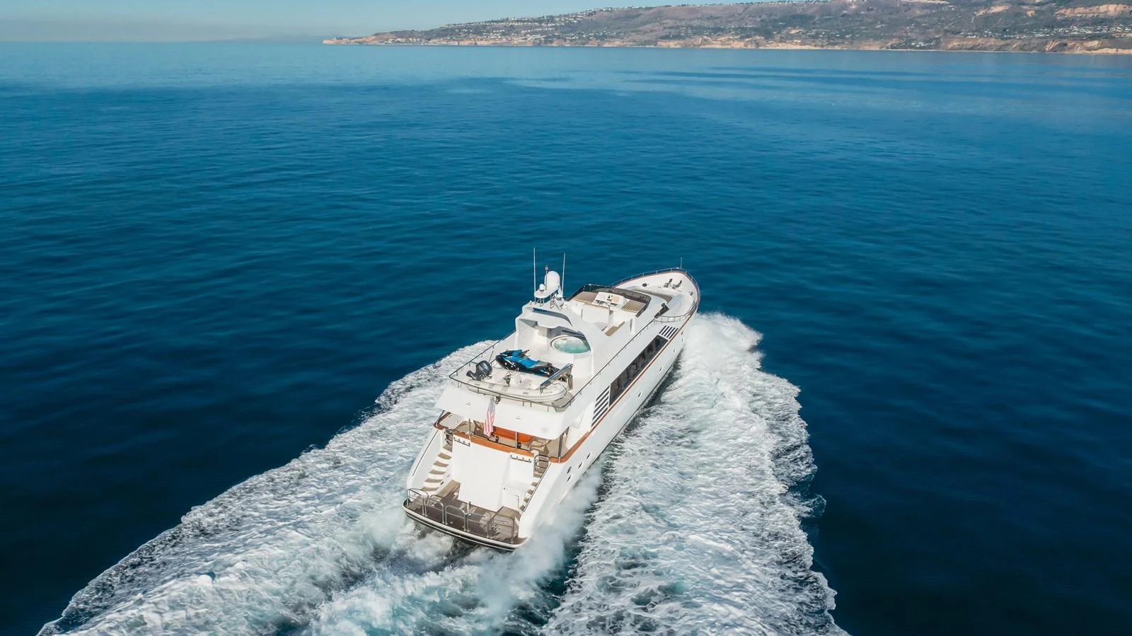 A luxurious yacht cruises through calm blue waters with a scenic coastline in the background. aboard MONEY CAT Yacht for Sale
