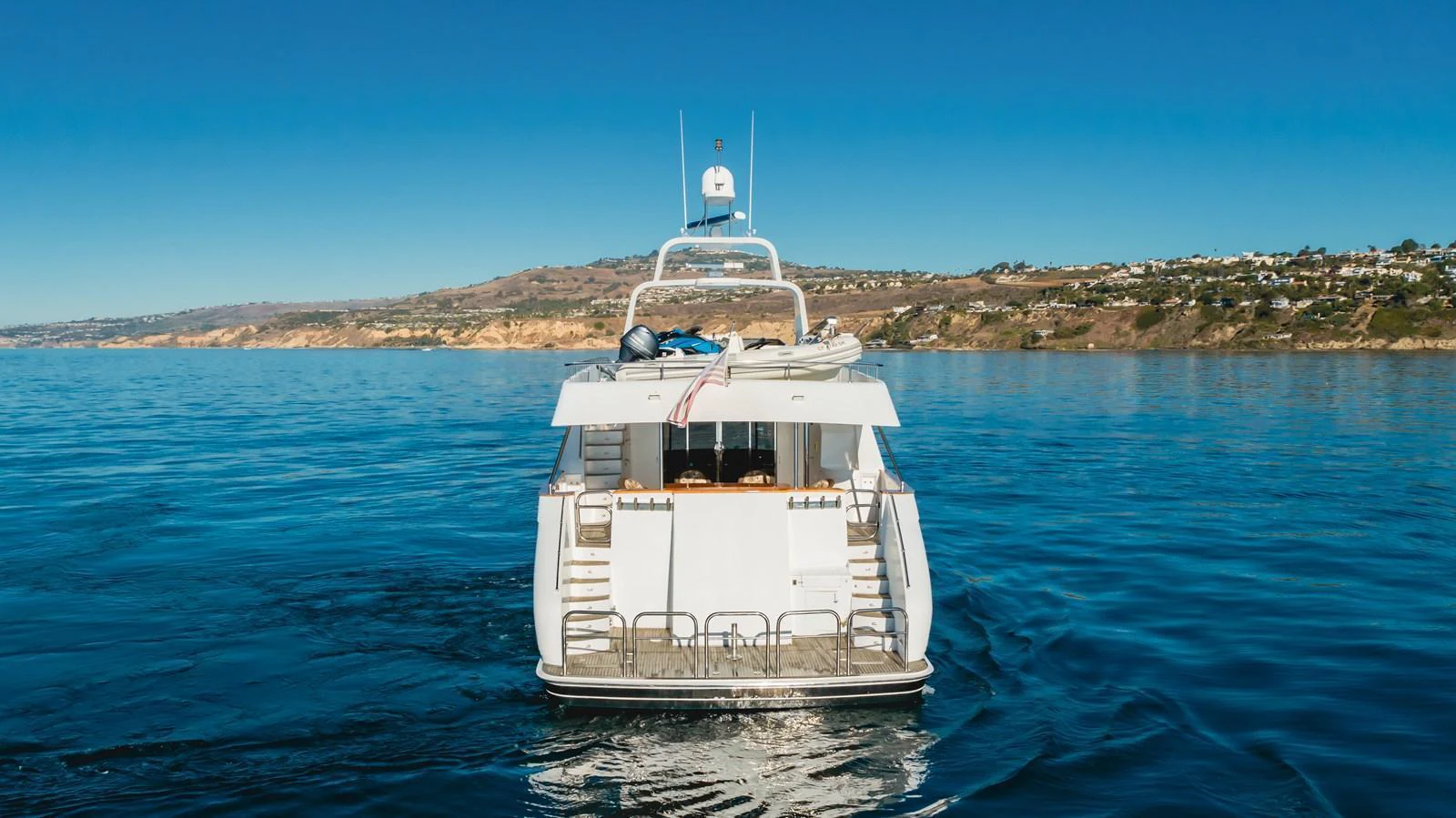 A luxurious yacht is seen from the rear, cruising on calm waters with a scenic coastline in the background. aboard MONEY CAT Yacht for Sale