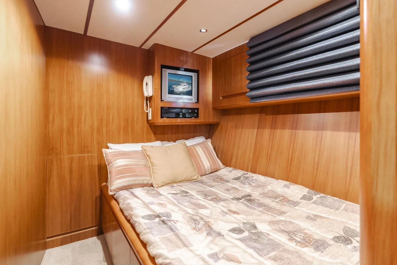 A cozy guest stateroom featuring a comfortable bed with patterned bedding and warm wood paneling. aboard MONEY CAT Yacht for Sale