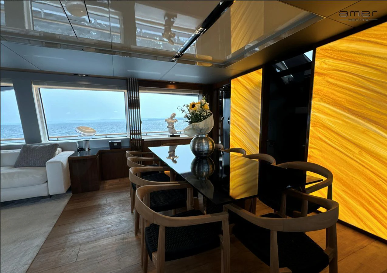 The yacht's dining area features a sleek black table surrounded by modern wooden chairs, with large windows offering a stunning ocean view. aboard ALTUS Yacht for Sale
