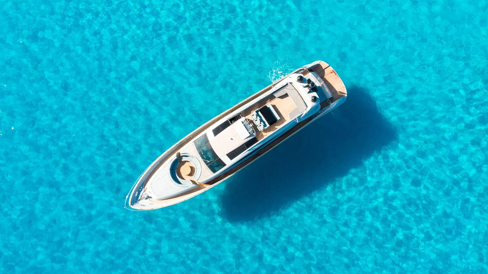 A sleek yacht floats gracefully on crystal-clear turquoise waters, viewed from above. aboard DEEA II Yacht for Sale