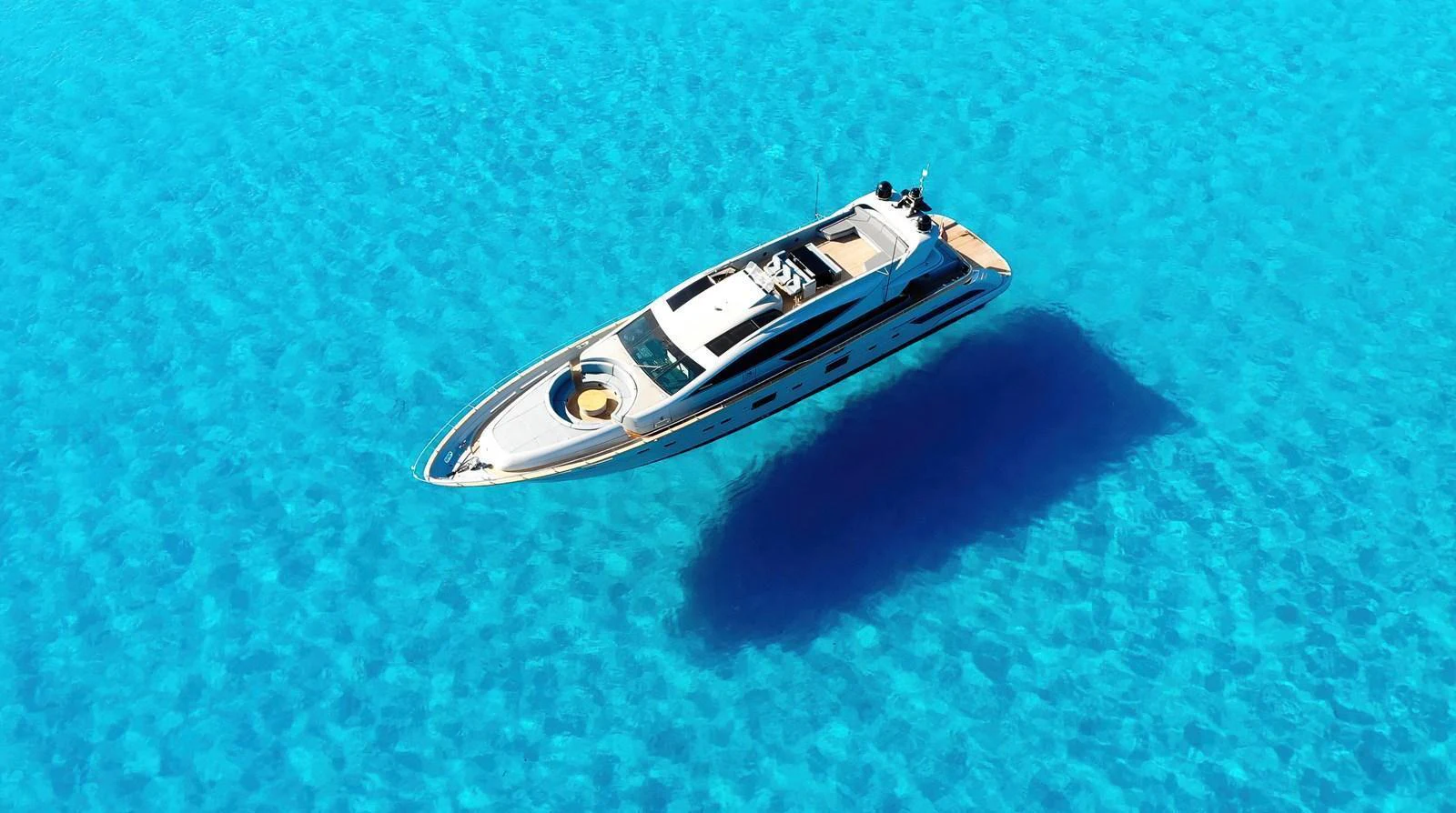 A sleek yacht glides over crystal-clear turquoise waters, casting a perfect shadow beneath. aboard DEEA II Yacht for Sale