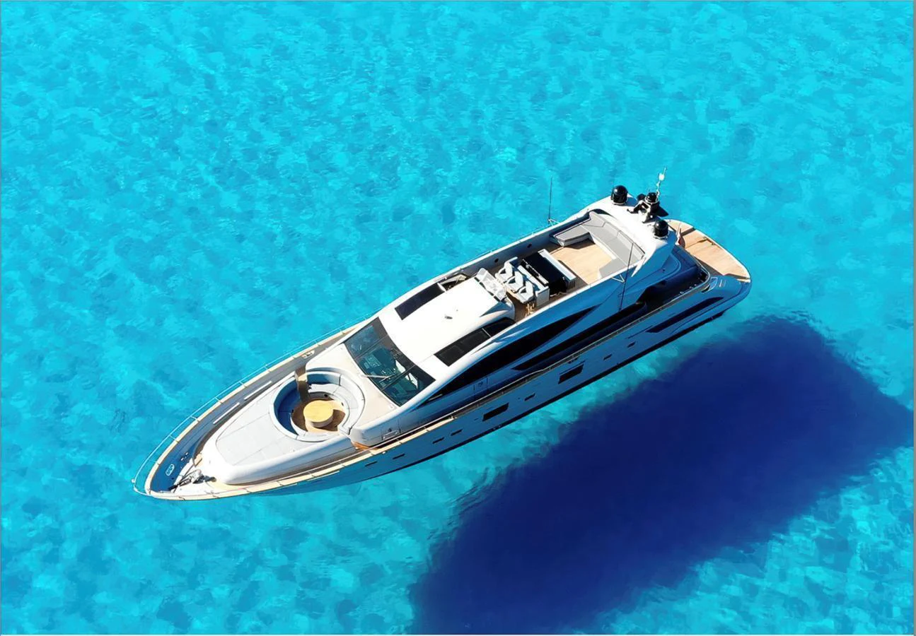 A sleek yacht glides gracefully over crystal-clear blue waters, showcasing its elegant design from an aerial perspective. aboard DEEA II Yacht for Sale