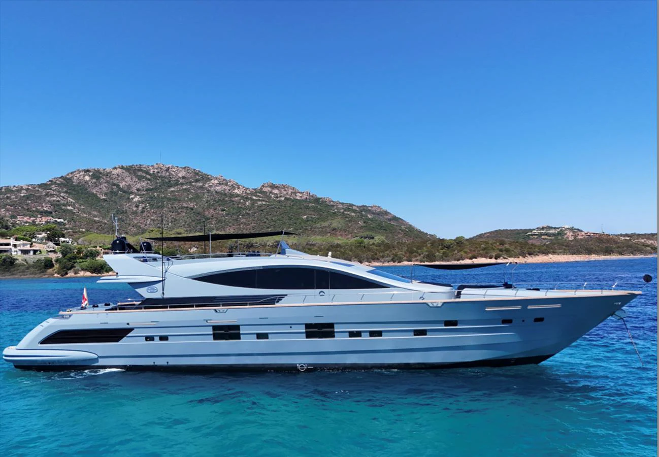A sleek and modern yacht glides gracefully on clear blue waters with a scenic mountainous backdrop. aboard DEEA II Yacht for Sale