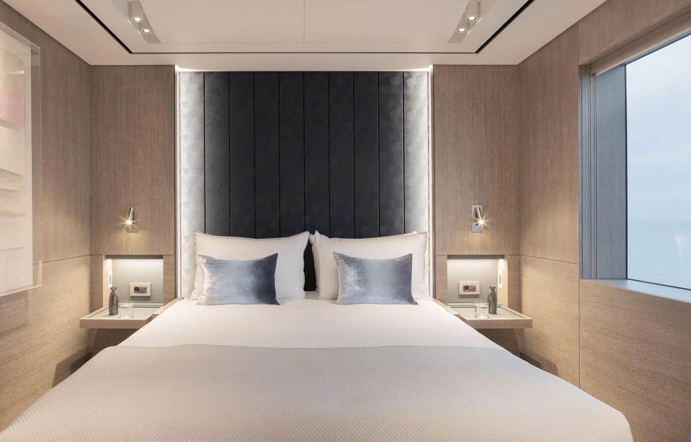 The stateroom features a luxurious bed with elegant lighting and large windows offering serene ocean views. aboard ENTOURAGE Yacht for Sale