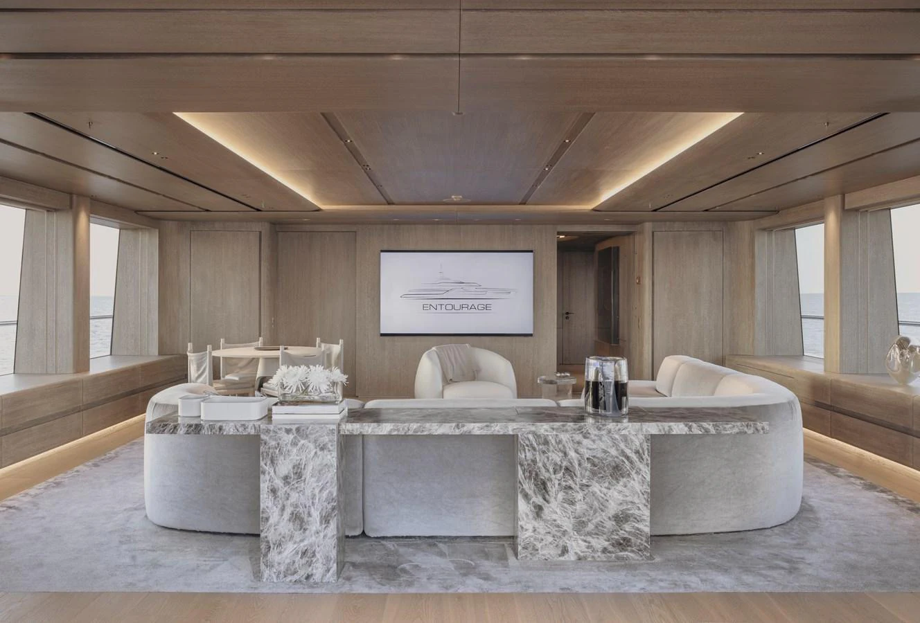 The yacht's salon features elegant seating and a sophisticated design with a large screen for entertainment. aboard ENTOURAGE Yacht for Sale