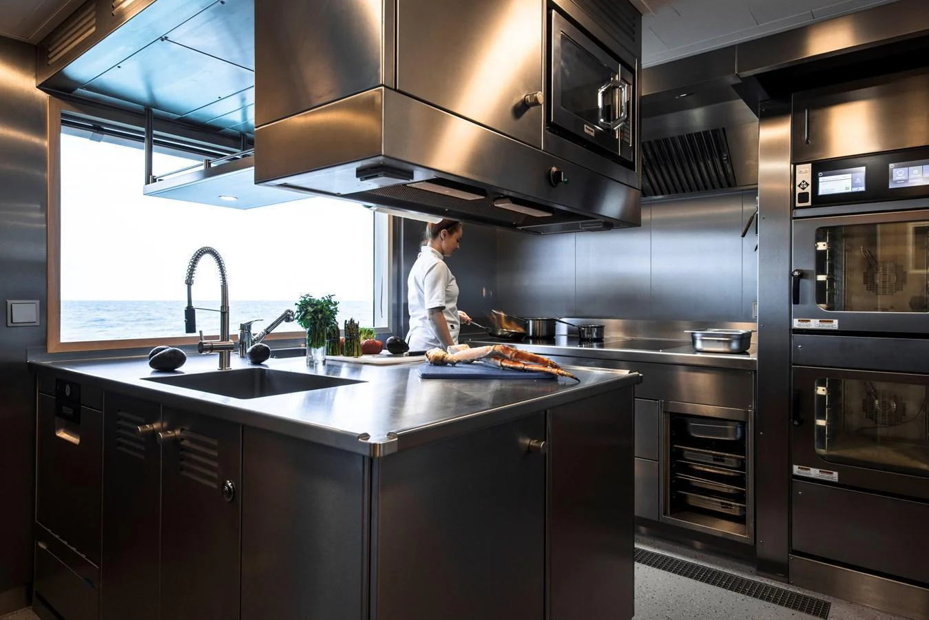 A modern yacht galley with stainless steel appliances and a chef preparing a meal. aboard ENTOURAGE Yacht for Sale