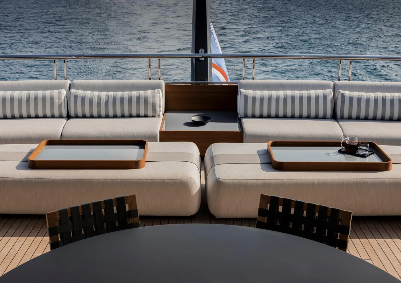 The aft deck features elegant seating with striped cushions and stylish wooden trays, offering a serene view of the water. aboard ENTOURAGE Yacht for Sale