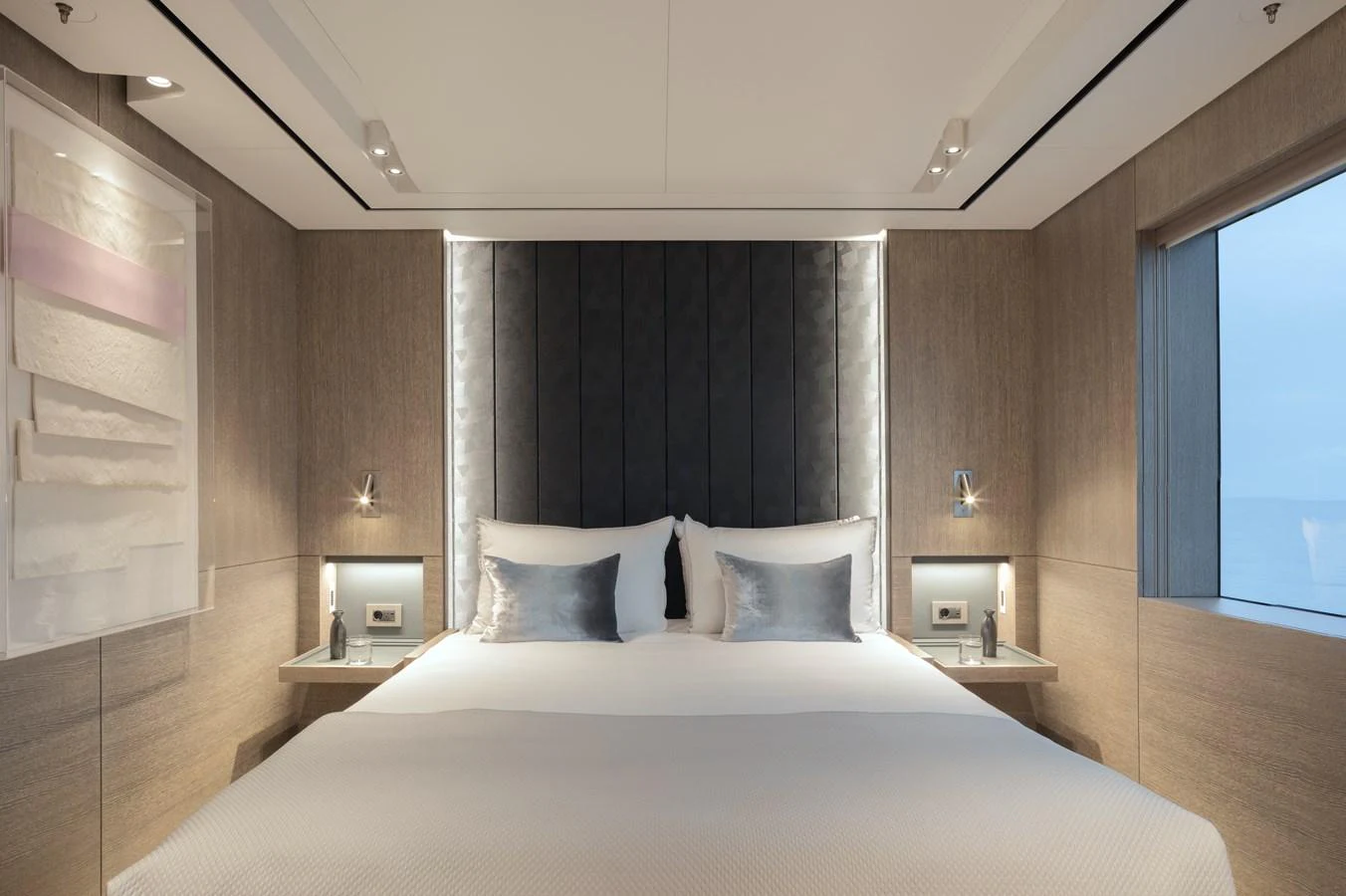 The stateroom features a luxurious bed with modern lighting and large windows offering serene ocean views. aboard ENTOURAGE Yacht for Sale