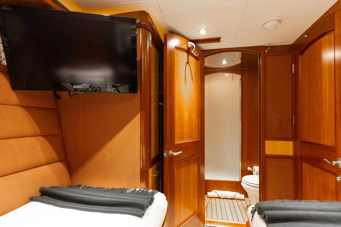 The guest cabin features twin beds, a wall-mounted TV, and an en-suite bathroom with wooden finishes. aboard AURELIA Yacht for Sale