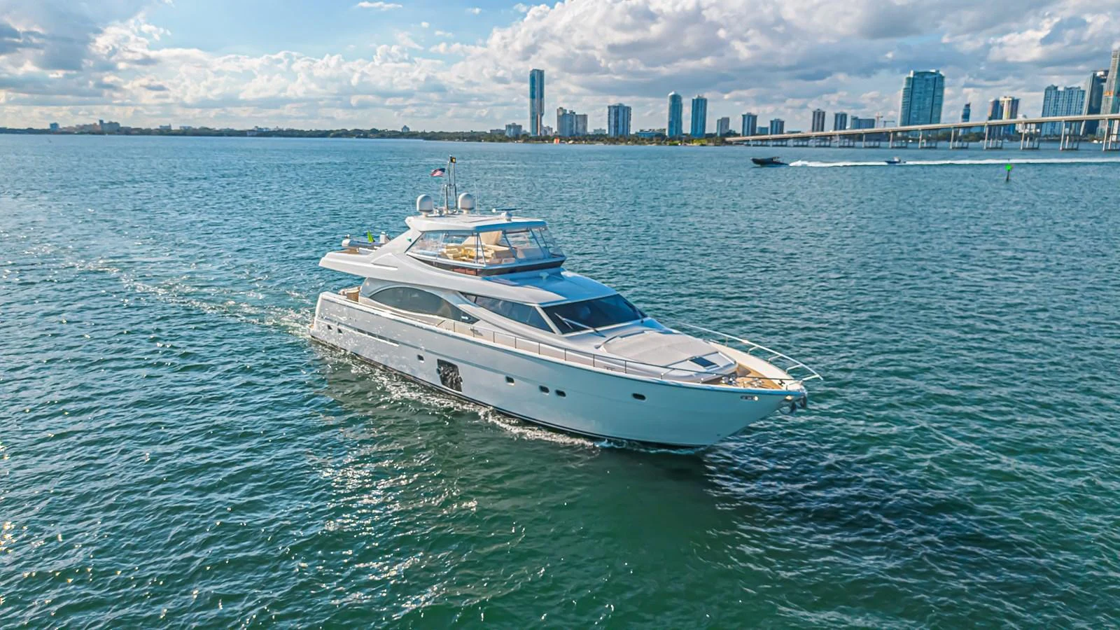 A sleek yacht cruises gracefully on calm waters with a city skyline in the background. aboard NORAL Yacht for Sale