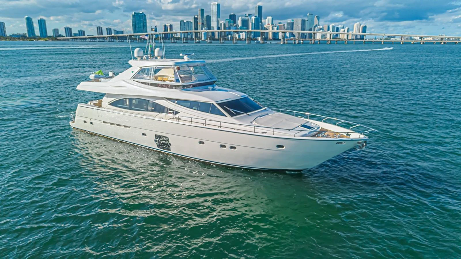 A sleek and modern yacht cruises gracefully on the water with a city skyline in the background. aboard NORAL Yacht for Sale