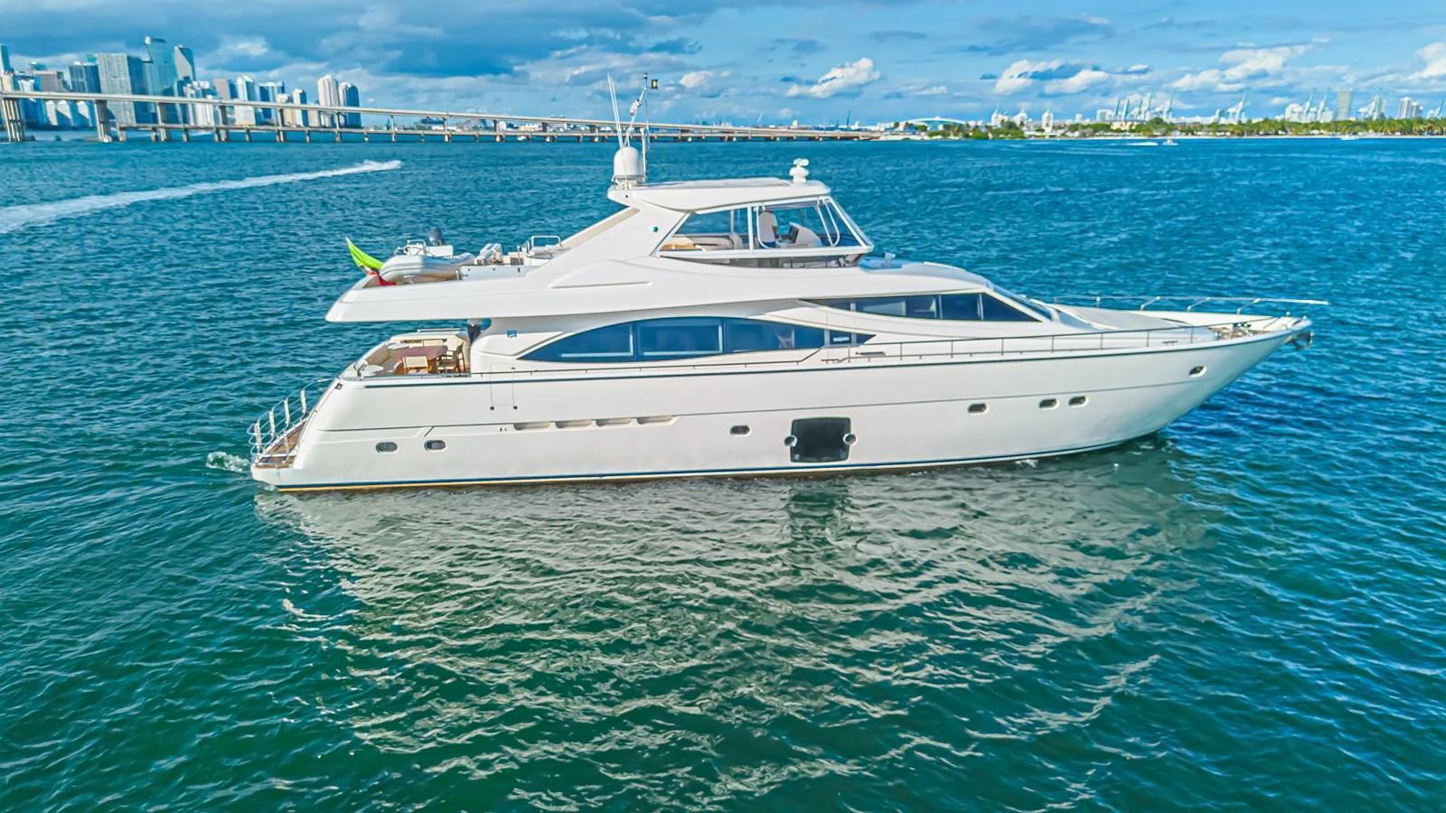 A sleek and elegant yacht cruising on calm waters with a cityscape in the background. aboard NORAL Yacht for Sale