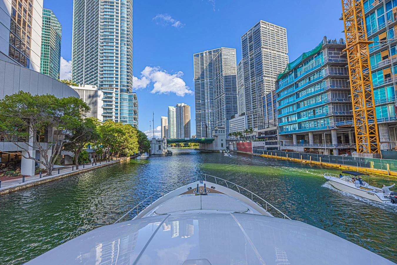 The yacht cruises through a vibrant cityscape, surrounded by towering buildings and clear blue skies. aboard NORAL Yacht for Sale