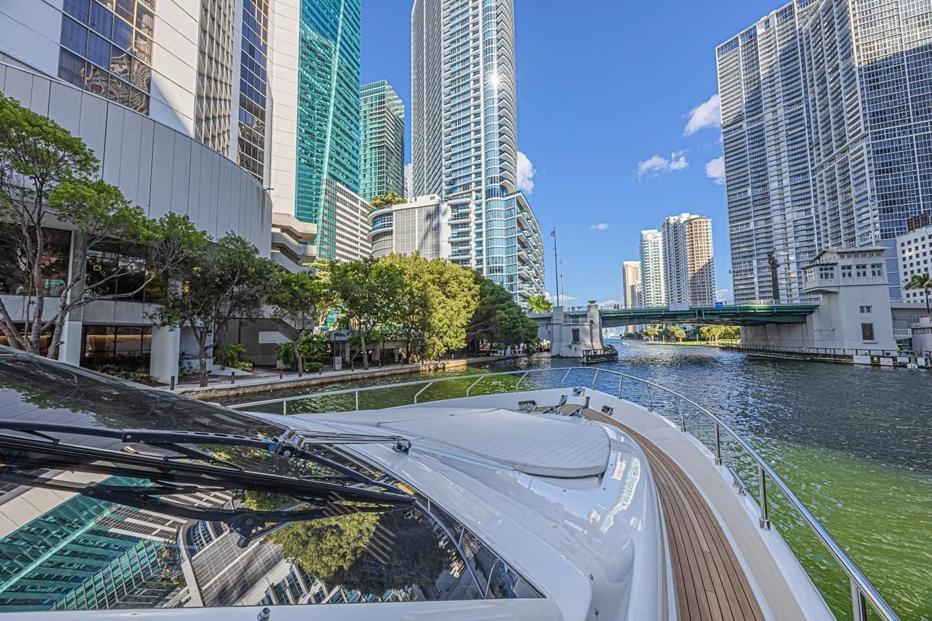 The yacht is cruising through a vibrant cityscape with modern high-rise buildings and a serene waterway. aboard NORAL Yacht for Sale