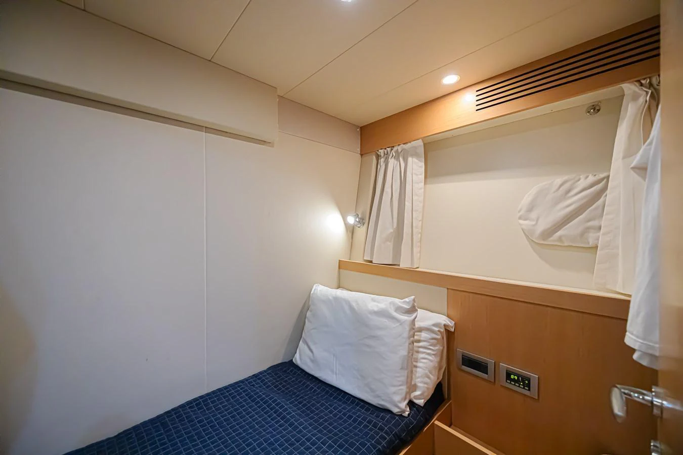 A cozy crew cabin featuring a single bed with a blue checkered blanket and white pillows. aboard NORAL Yacht for Sale