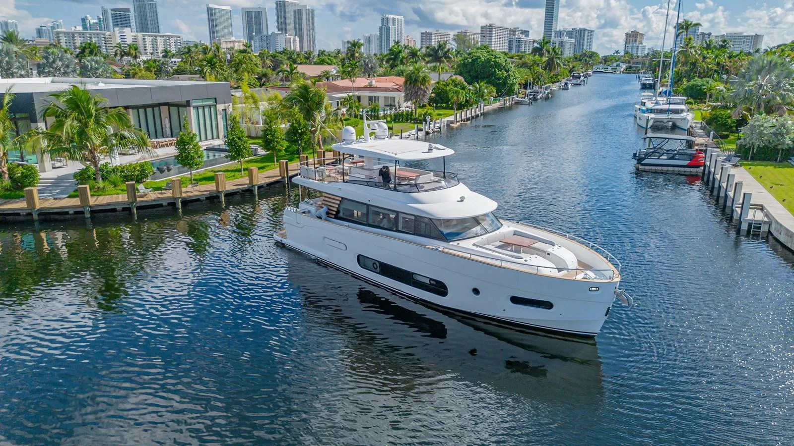 A sleek yacht cruises through a serene canal with modern buildings in the background. aboard XAX66M61L122 Yacht for Sale