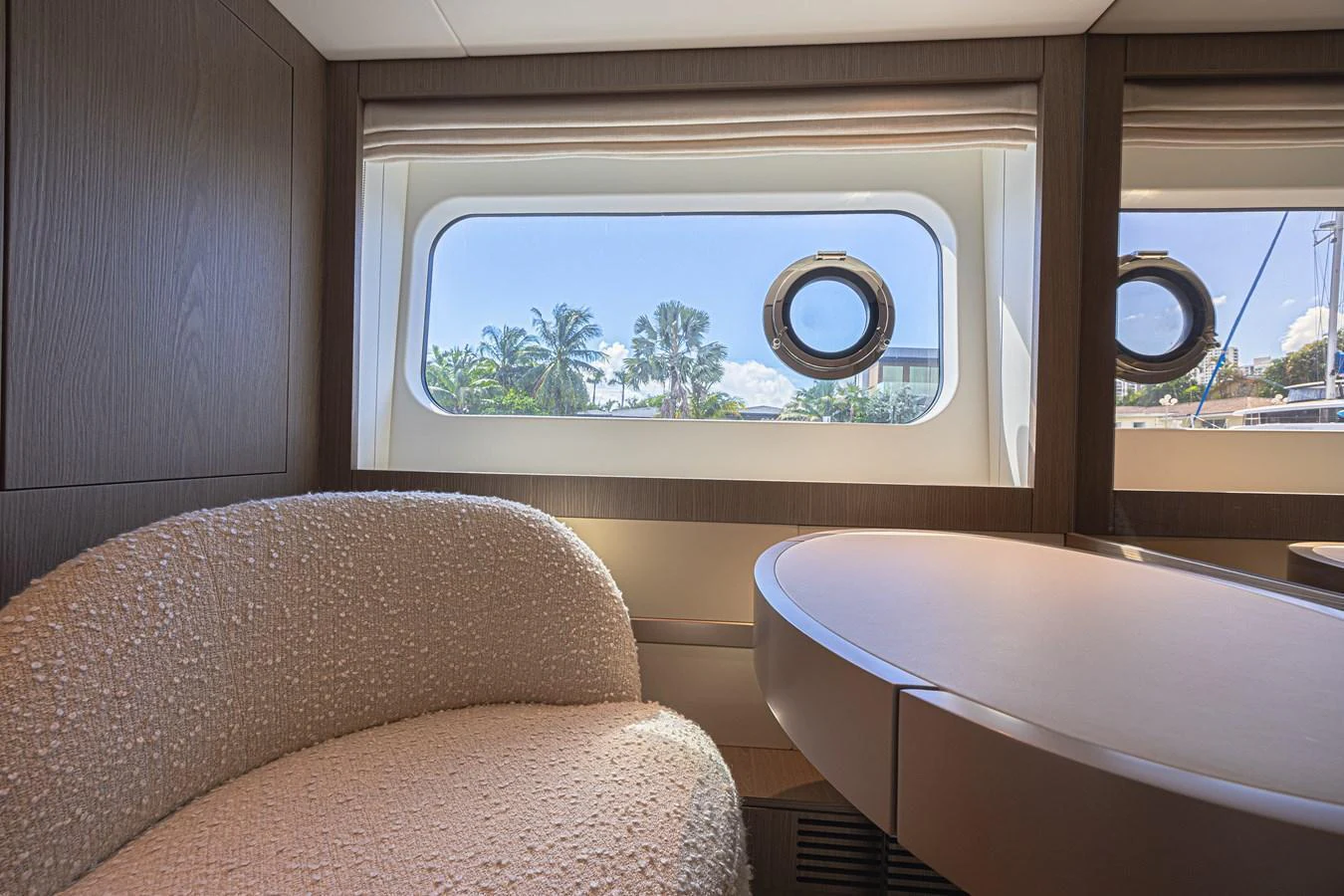 A cozy seating area with a round table and a window offering a view of palm trees. aboard XAX66M61L122 Yacht for Sale