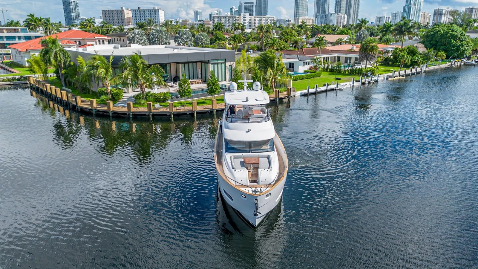A luxurious yacht cruises through a serene canal with a backdrop of modern waterfront homes. aboard XAX66M61L122 Yacht for Sale