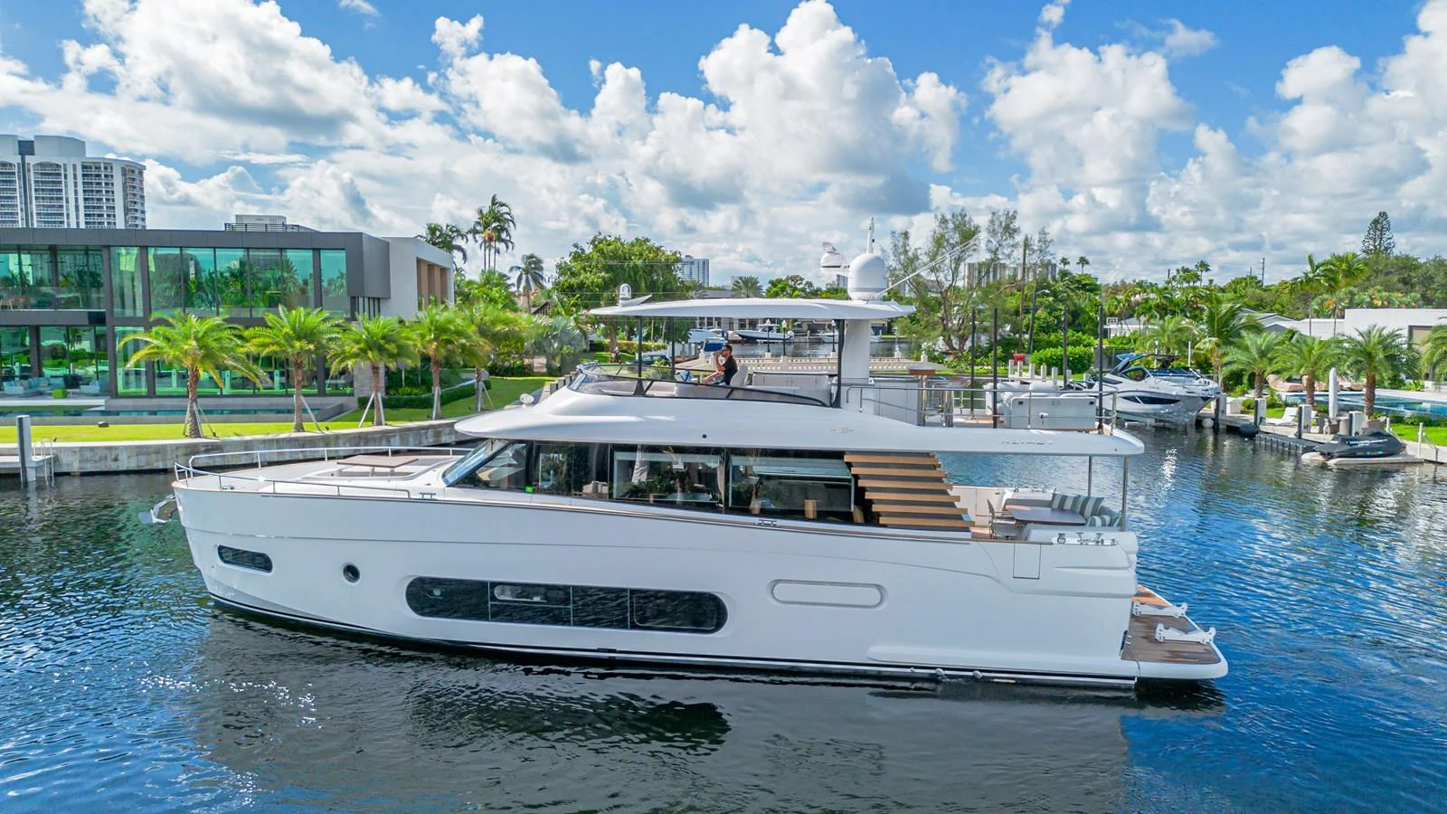 A sleek and modern yacht is docked in a serene marina with lush greenery and contemporary buildings in the background. aboard XAX66M61L122 Yacht for Sale