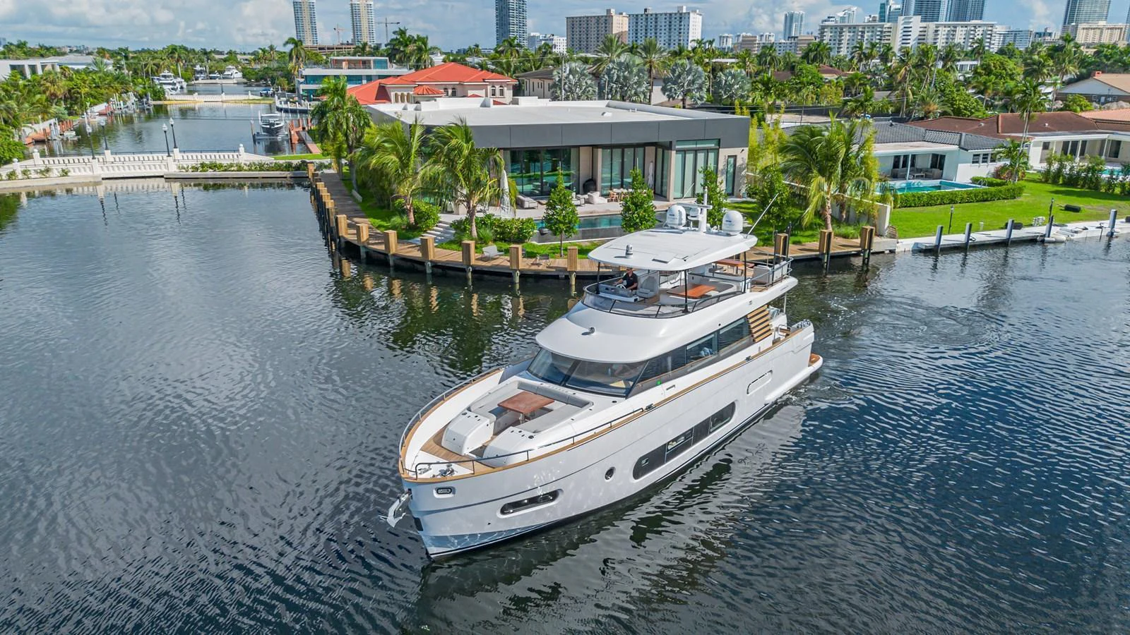 A sleek and modern yacht cruises through a serene waterfront neighborhood. aboard XAX66M61L122 Yacht for Sale
